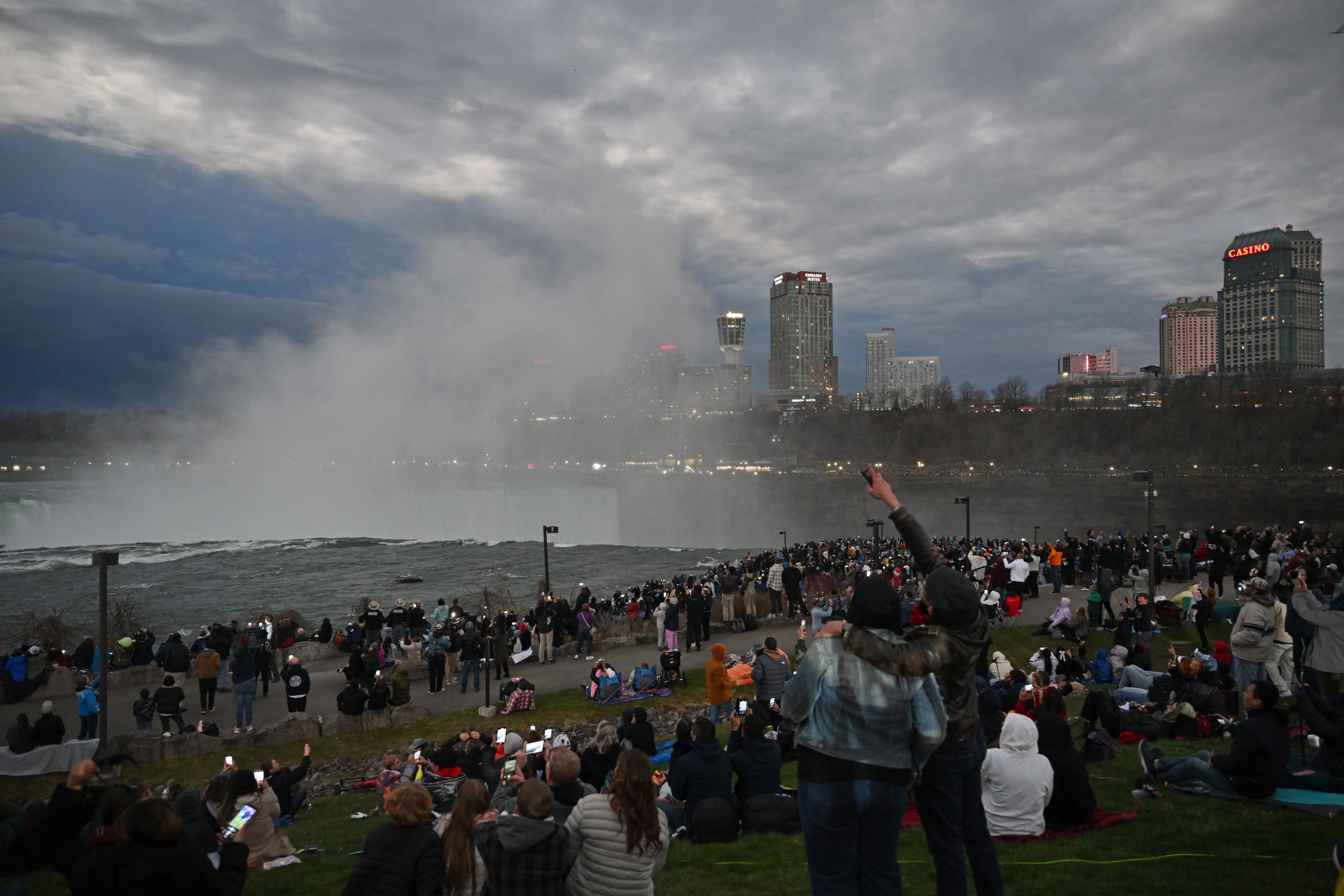 The sky darkens as people look up at the sun during the total solar eclipse across North America, at Niagara Falls State Park in Niagara Falls, New York, on April 8, 2024. This year's path of totality is 115 miles (185 kilometers) wide and home to nearly 32 million Americans, with an additional 150 million living less than 200 miles from the strip. The next total solar eclipse that can be seen from a large part of North America won't come around until 2044. (Photo by ANGELA WEISS / AFP) (Photo by ANGELA WEISS/AFP via Getty Images)