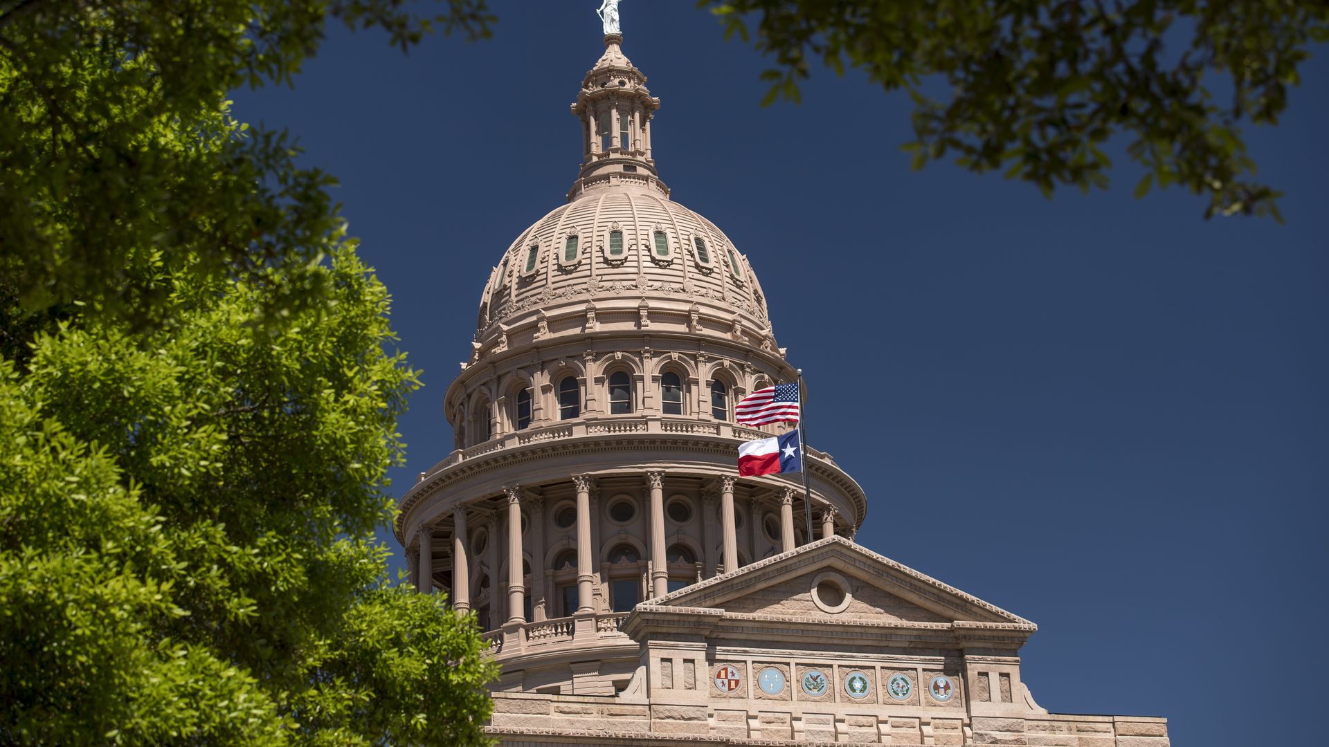 Photo of the Texas State Capitol as the state flag flies beside the American flag on top of the entrance