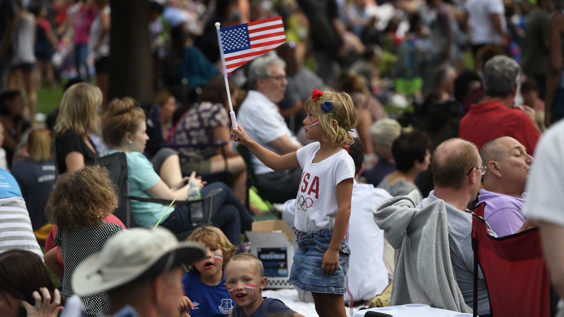 A child in a white shirt with USA on it raises an American flag