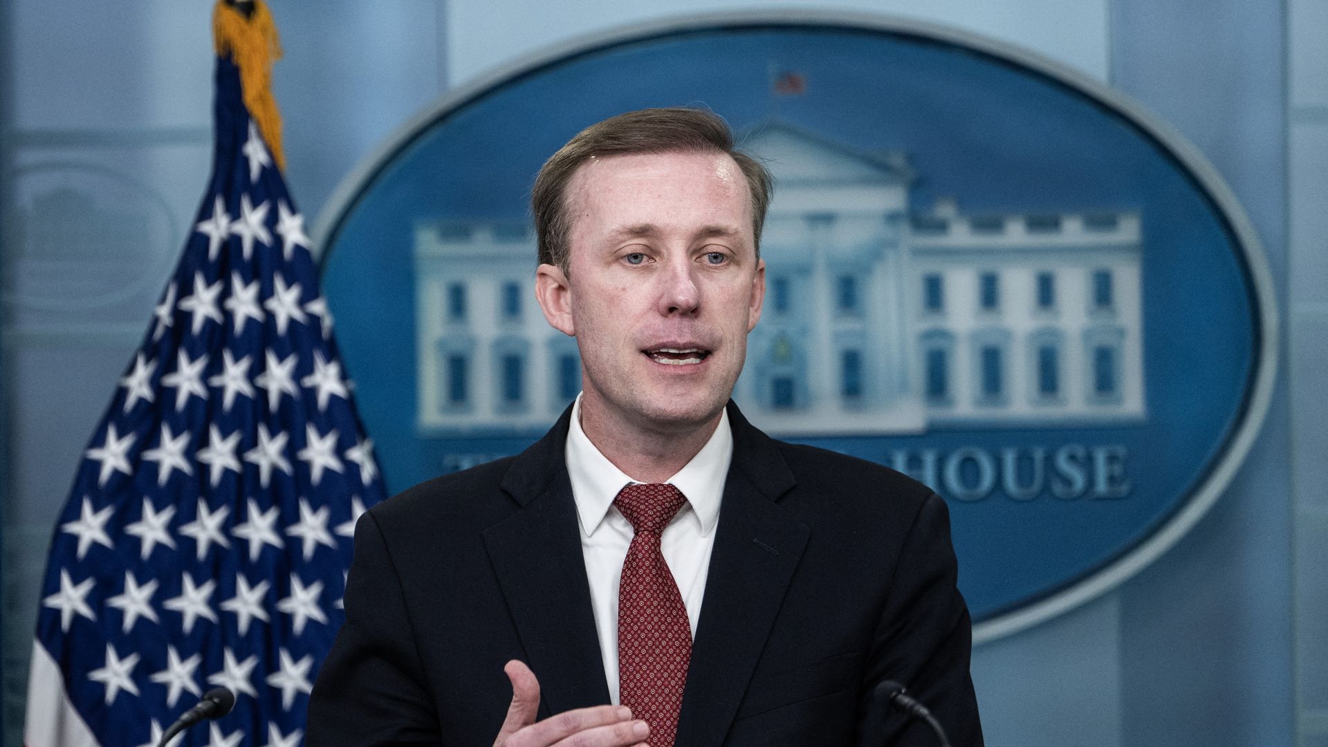 Jake Sullivan speaks in front of a U.S. flag and a White House logo.