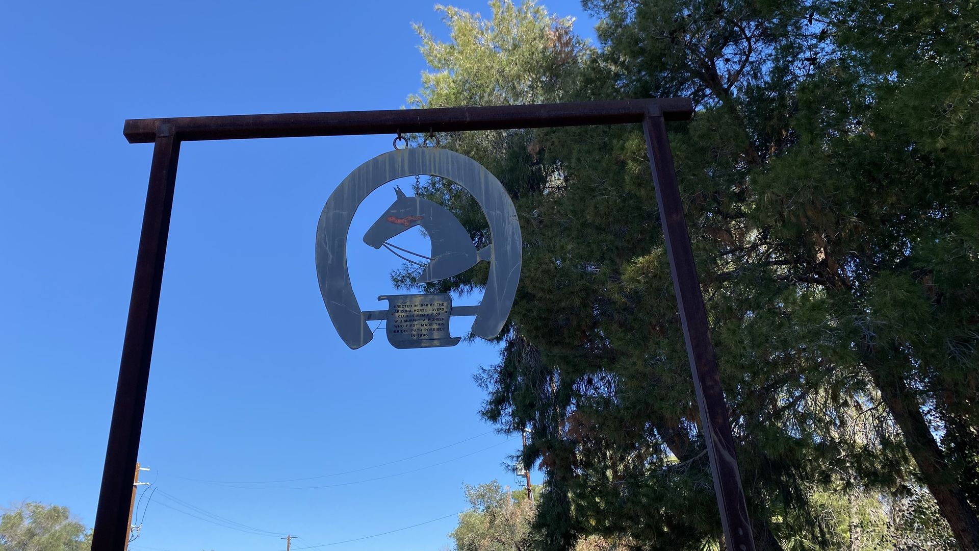 A flat metal image of a horse's head inside a horseshoe that's hanging from a crossbeam.