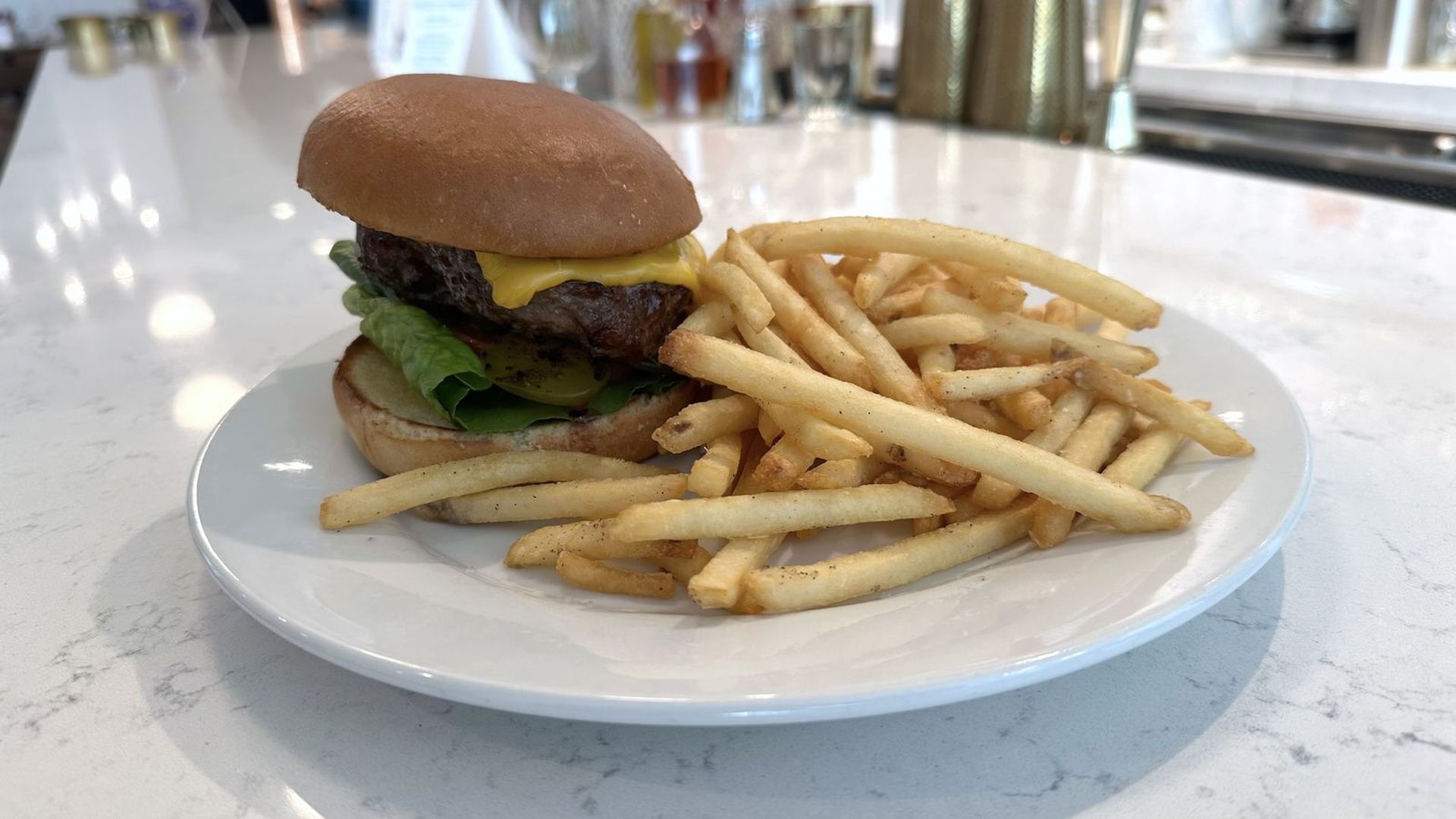 A cheeseburger and fries sits on a plate atop a marble bar.
