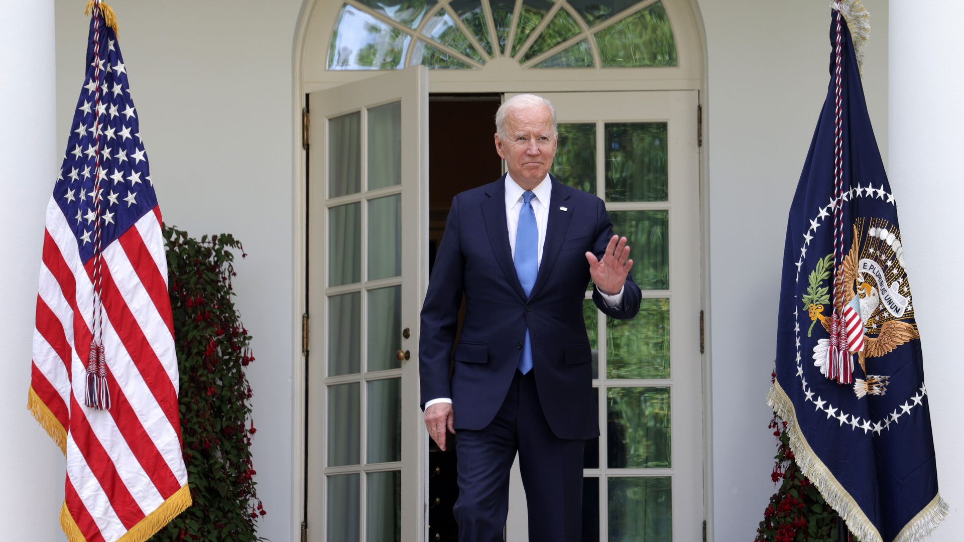 BIden stands between two flags at the White House and waves