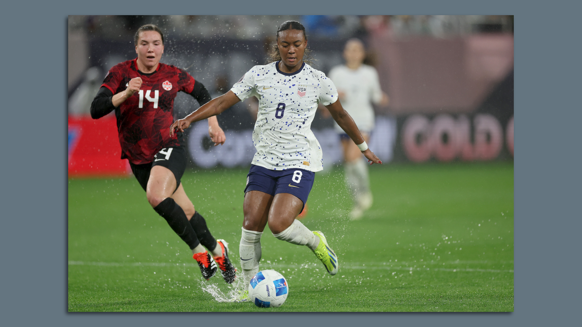 USWNT forward Jaedyn Shaw shoots a soccer ball splashing in a puddle on the field. 