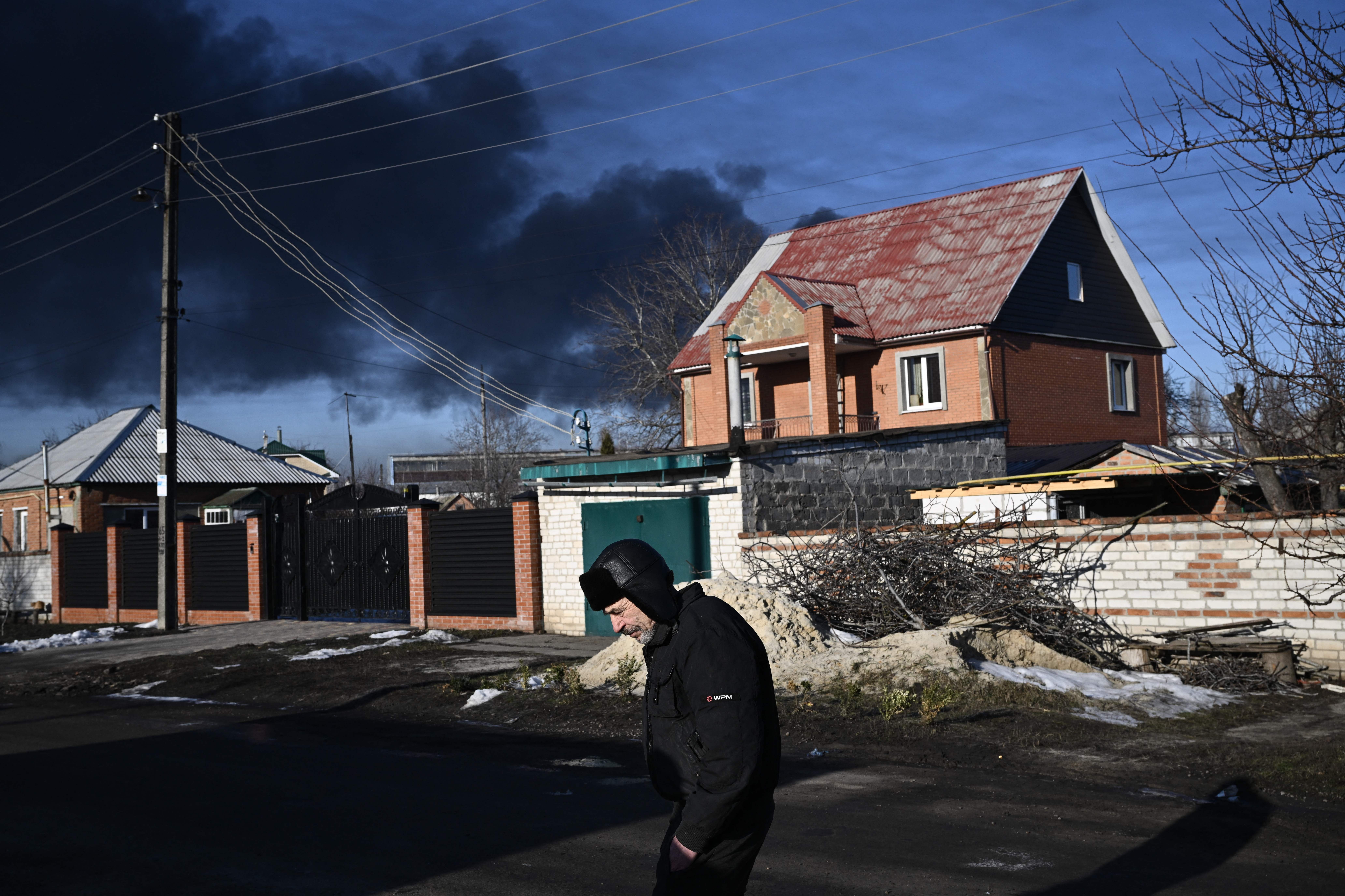 A man walks in a street as black smoke rises from a military airport in Chuguyev near Kharkiv on February 24.