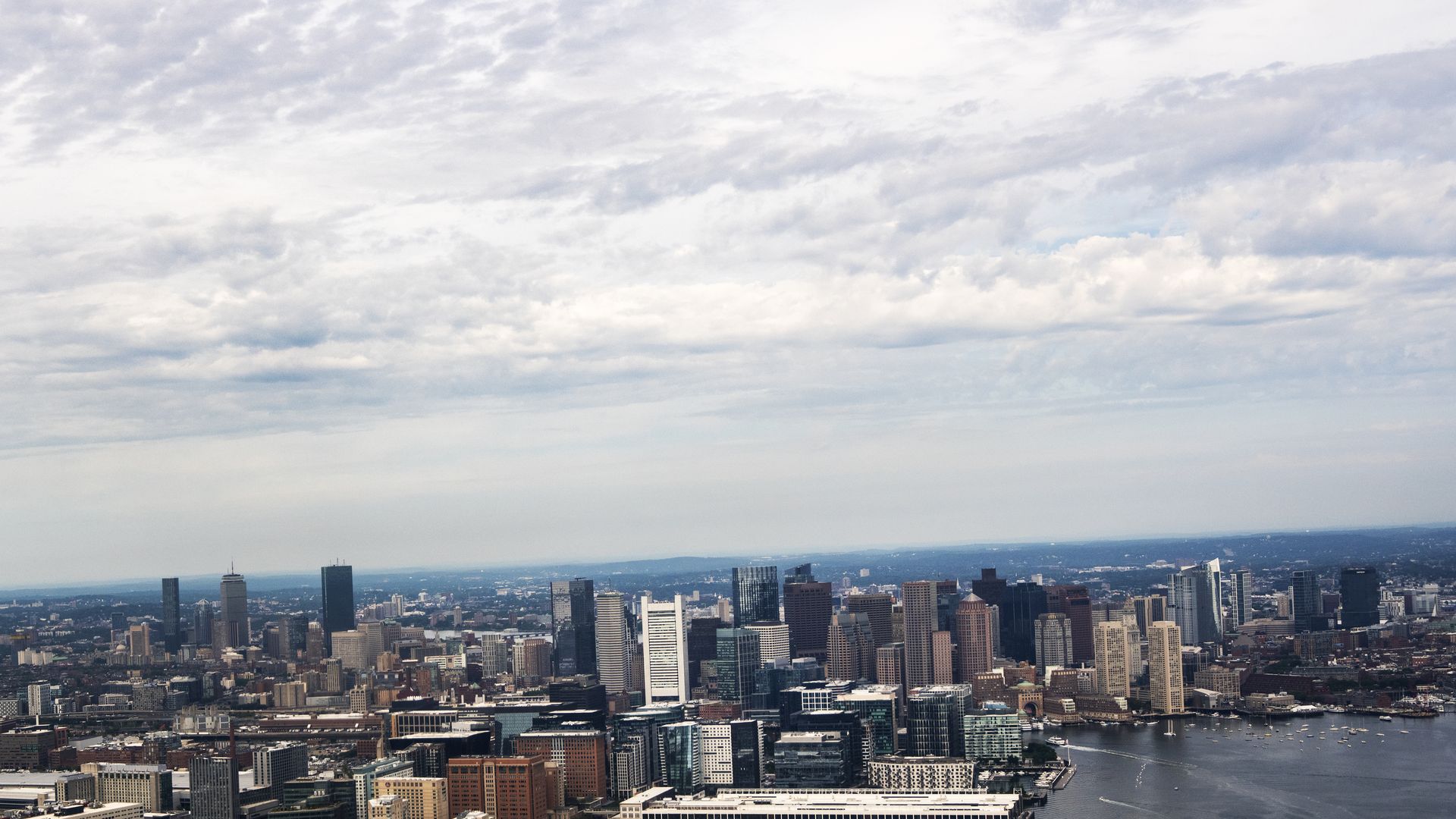 Aerial view of a city skyline with tall buildings near a large body of water, under a partly cloudy sky during daytime.