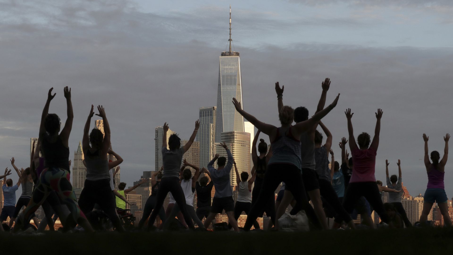 Silhouettes of people doing a yoga on a pier facing Lower Manhattan