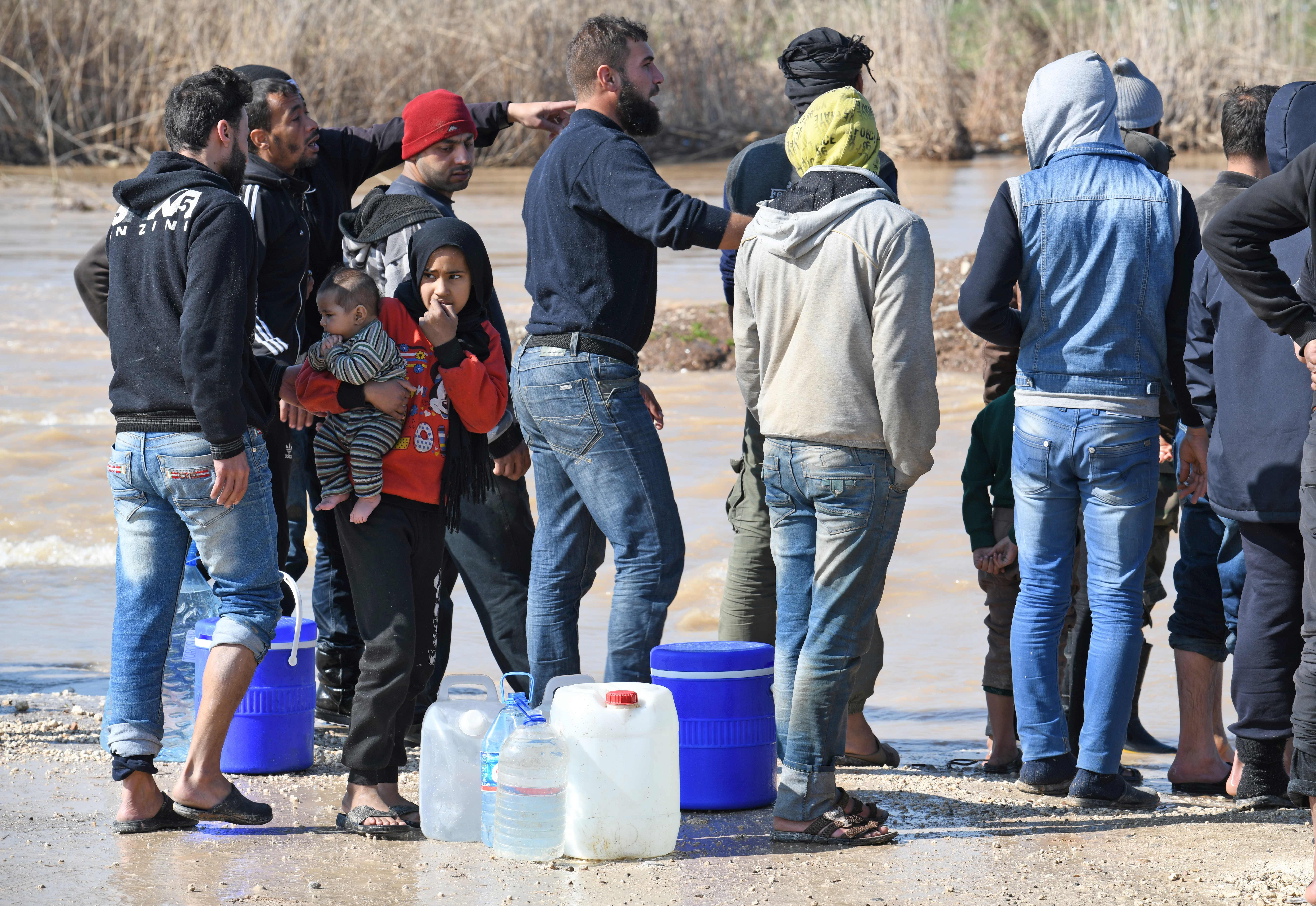 Syrian displaced people wait to carry water canisters in the flooded Deir al-Ballut refugee camp in Afrin's countryside