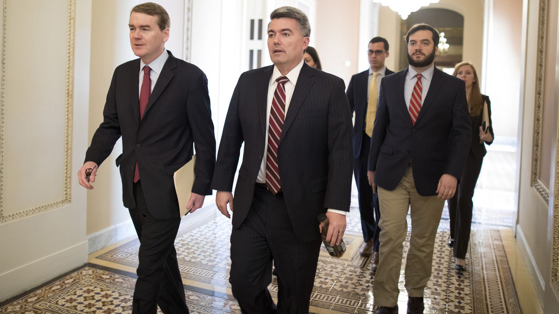 Sen. Michael Bennett and Sen. Cory Gardner walk down a hallway together 