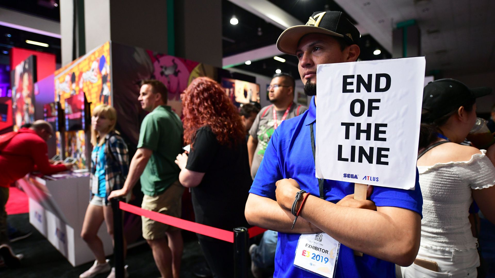Photo of people standing in line at a convention center. On the right, a person holds a sign that reads: 'end of the line'