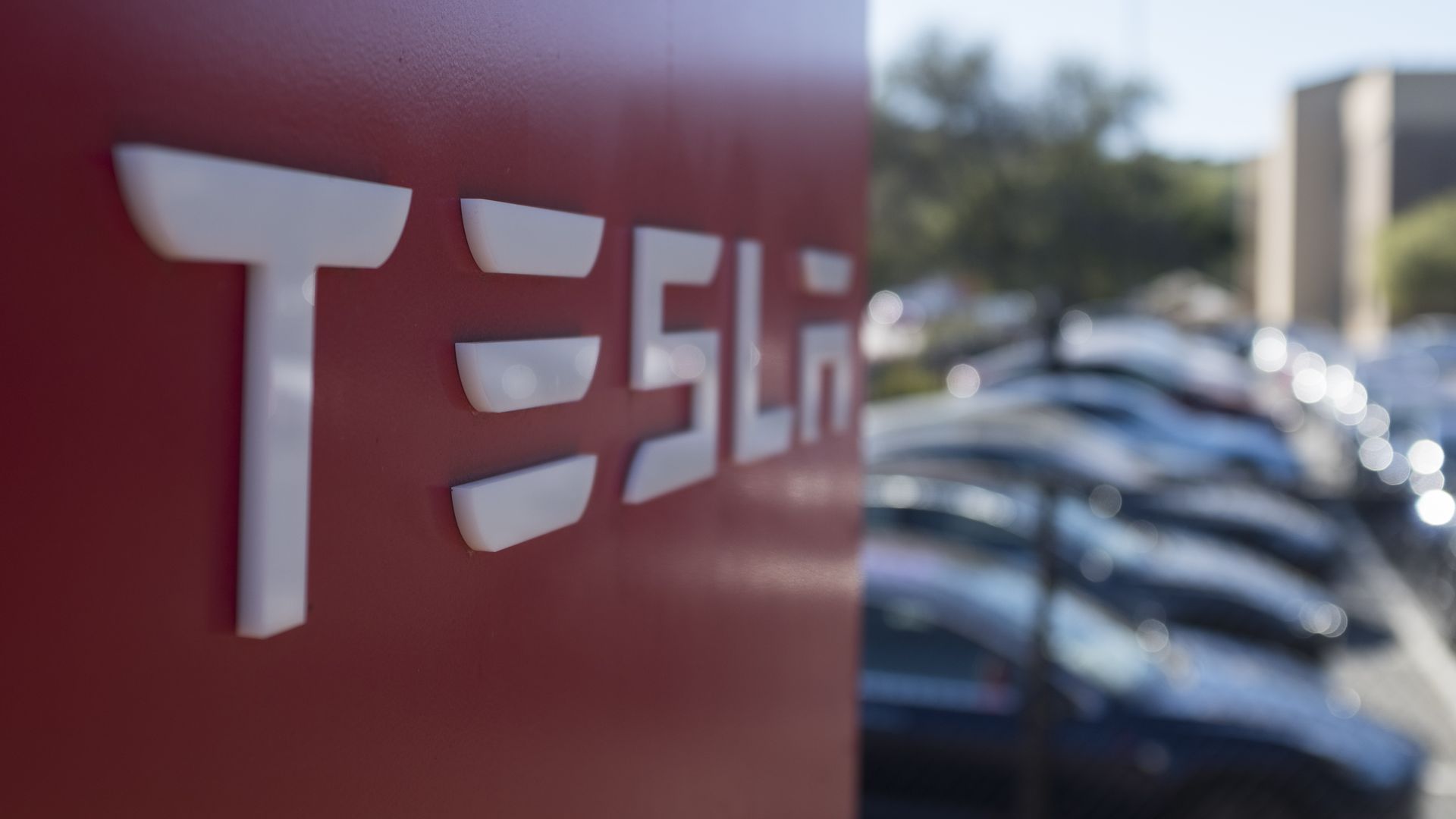 Photo of a red Tesla sign next to a parking lot filled with cars