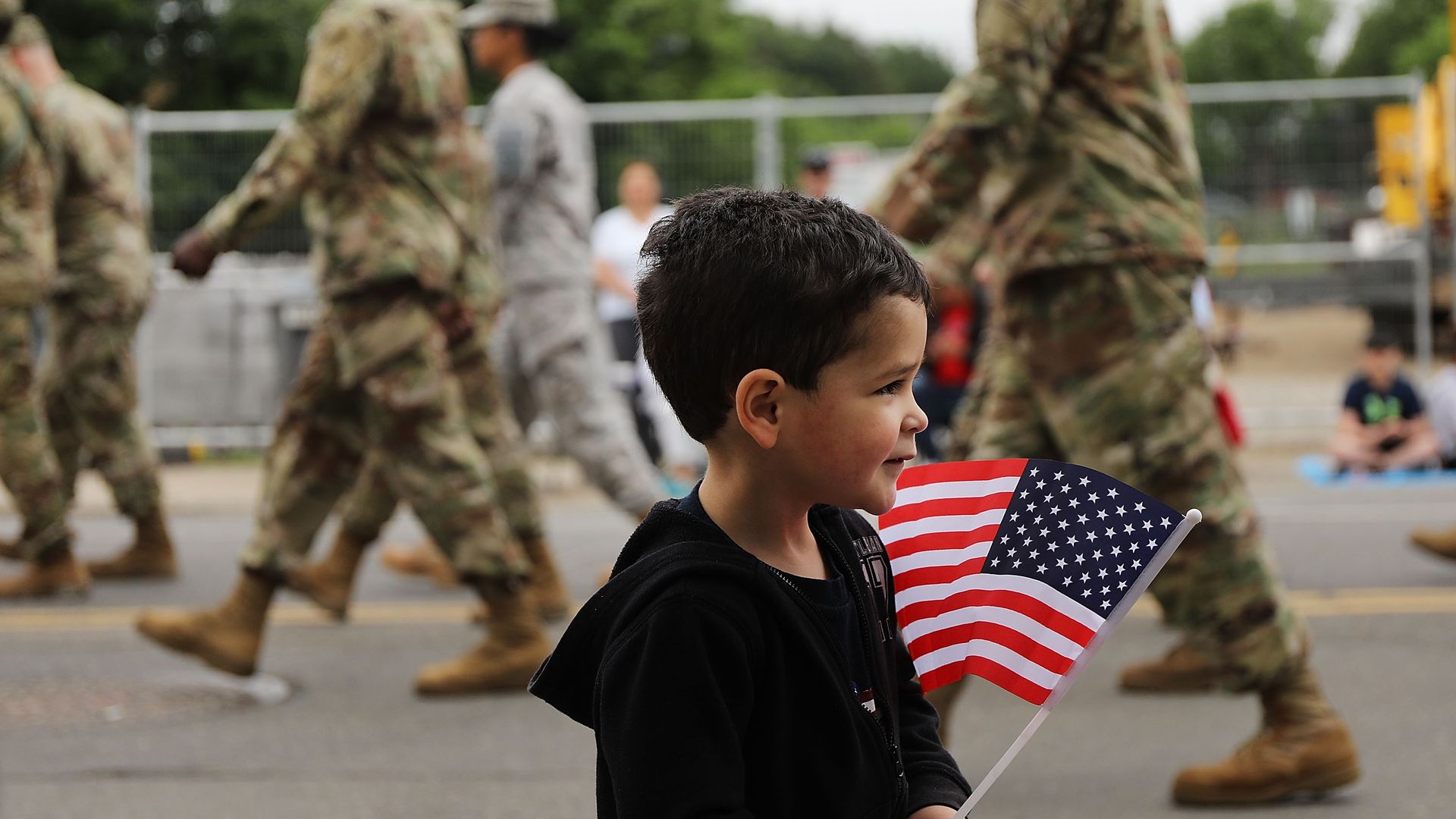 A child holding an American flag while U.S. soldiers walk by.