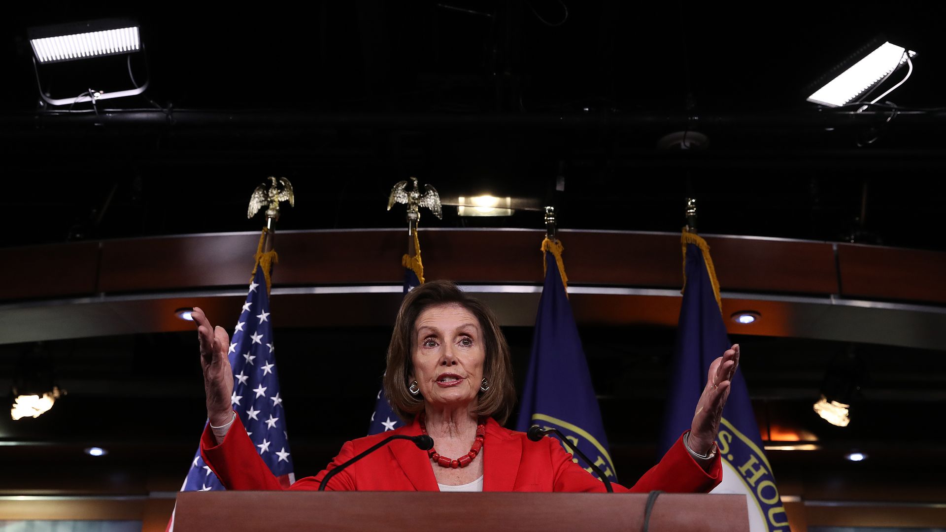 In this image, Nancy Pelosi stands behind a podium and speaks.