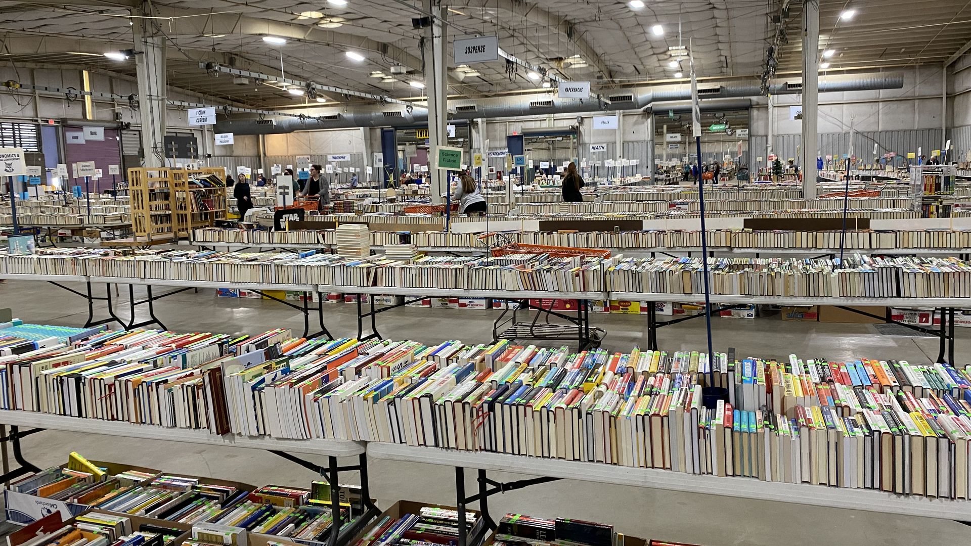 Tables covered in thousands of books in a warehouse-sized room.