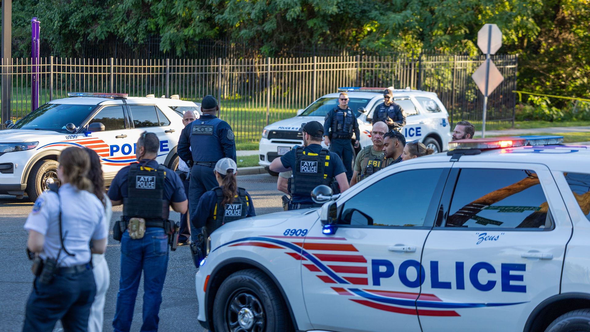 Several law enforcement officers and police cars are seen on a street during the daytime 