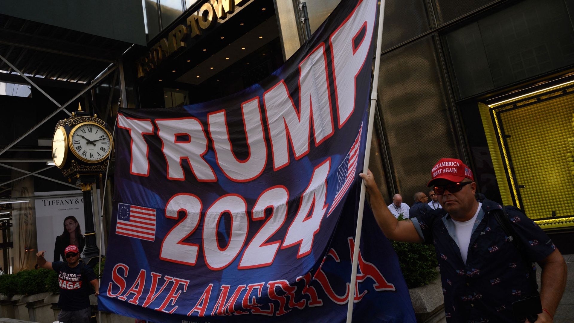 People hold a banner reading "Trump 2024" outside of the Trump Tower.