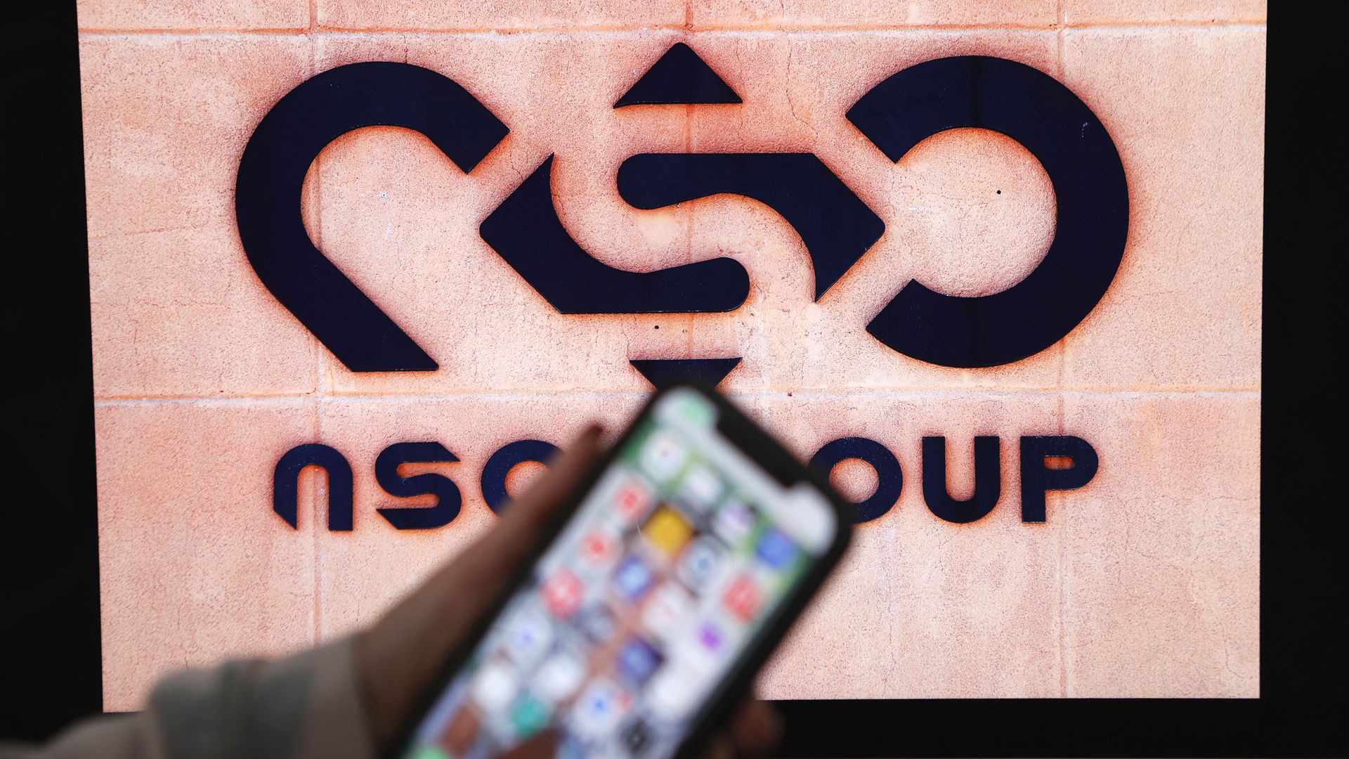 A photo illustration of a blurry smartphone in front of an NSO Group sign