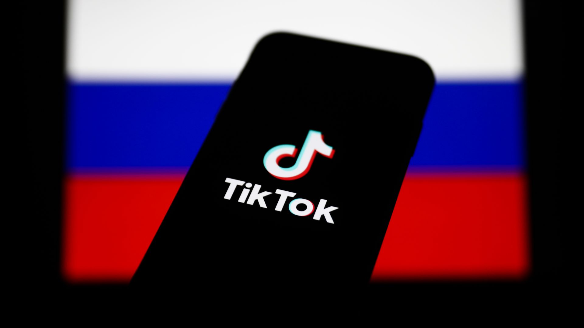 a photo of tik tok logo on a phone in front of russia flag