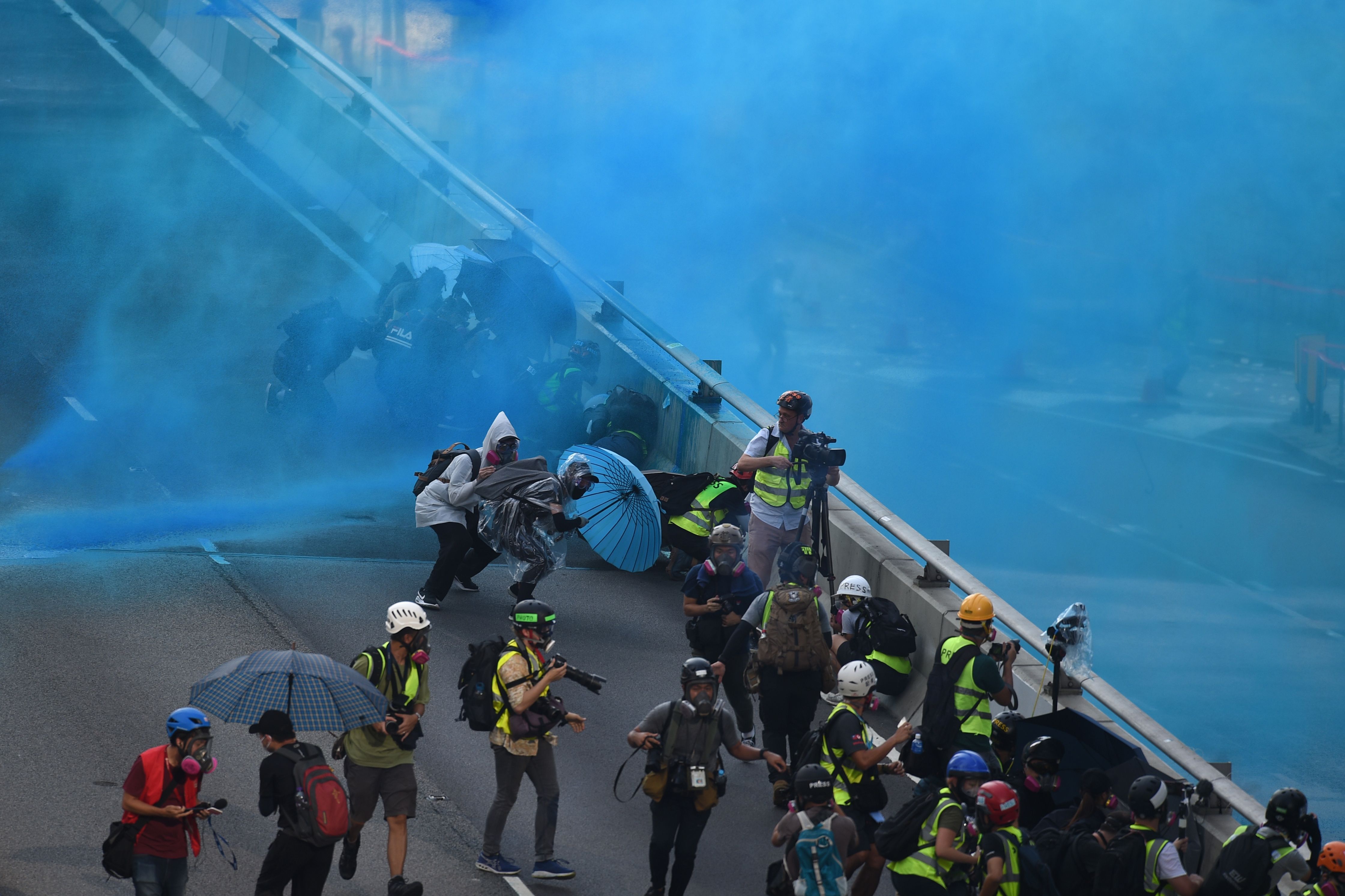 Members of the media (in yellow vests) look on as Hong Kong police fire water cannon from the central government complex