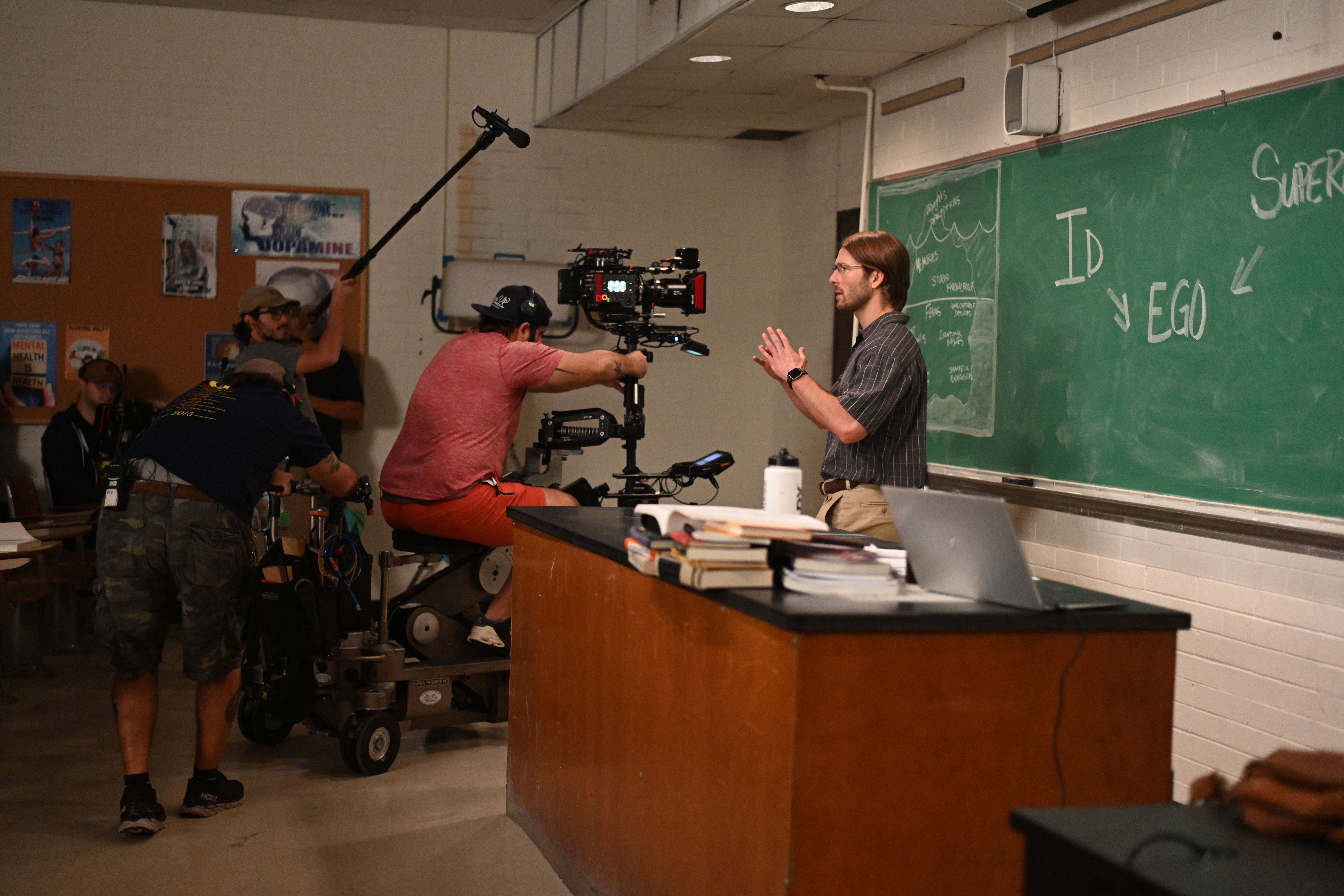 Photo shows Glen Powell teaching in a UNO classroom with a camera crew in front of him.
