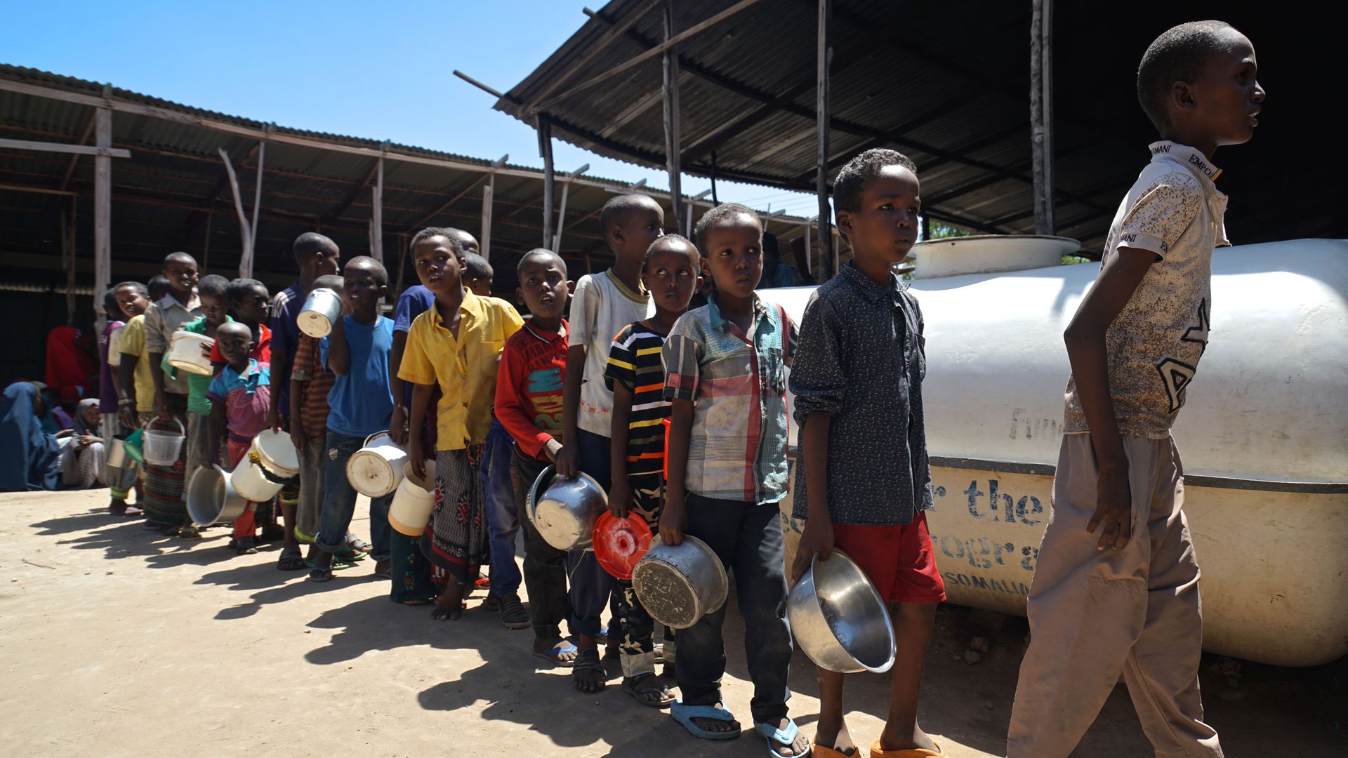 Somali boys in a line, carrying metal dishes