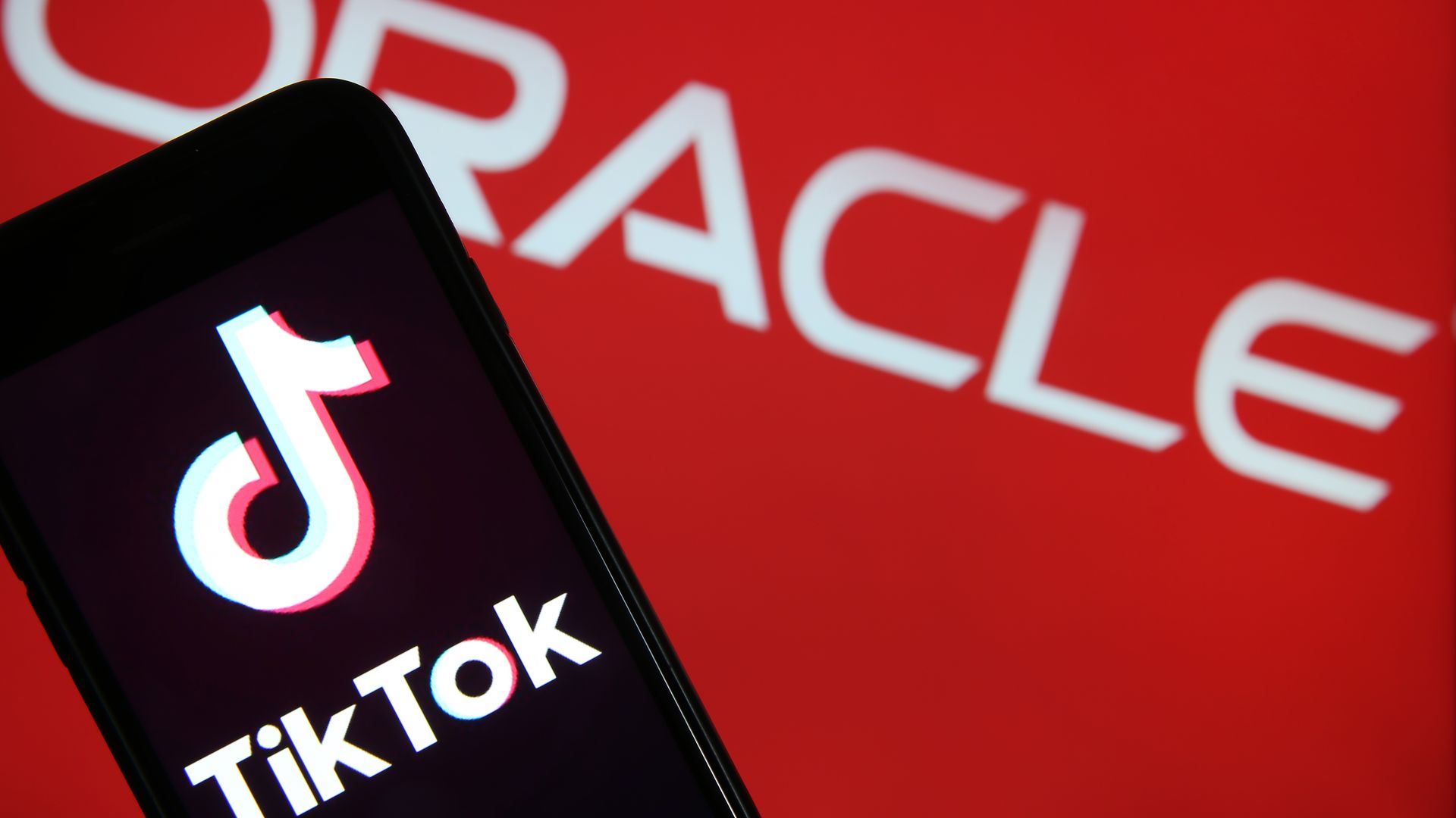A photo of a phone displaying the TikTok logo, held in front of the Oracle logo