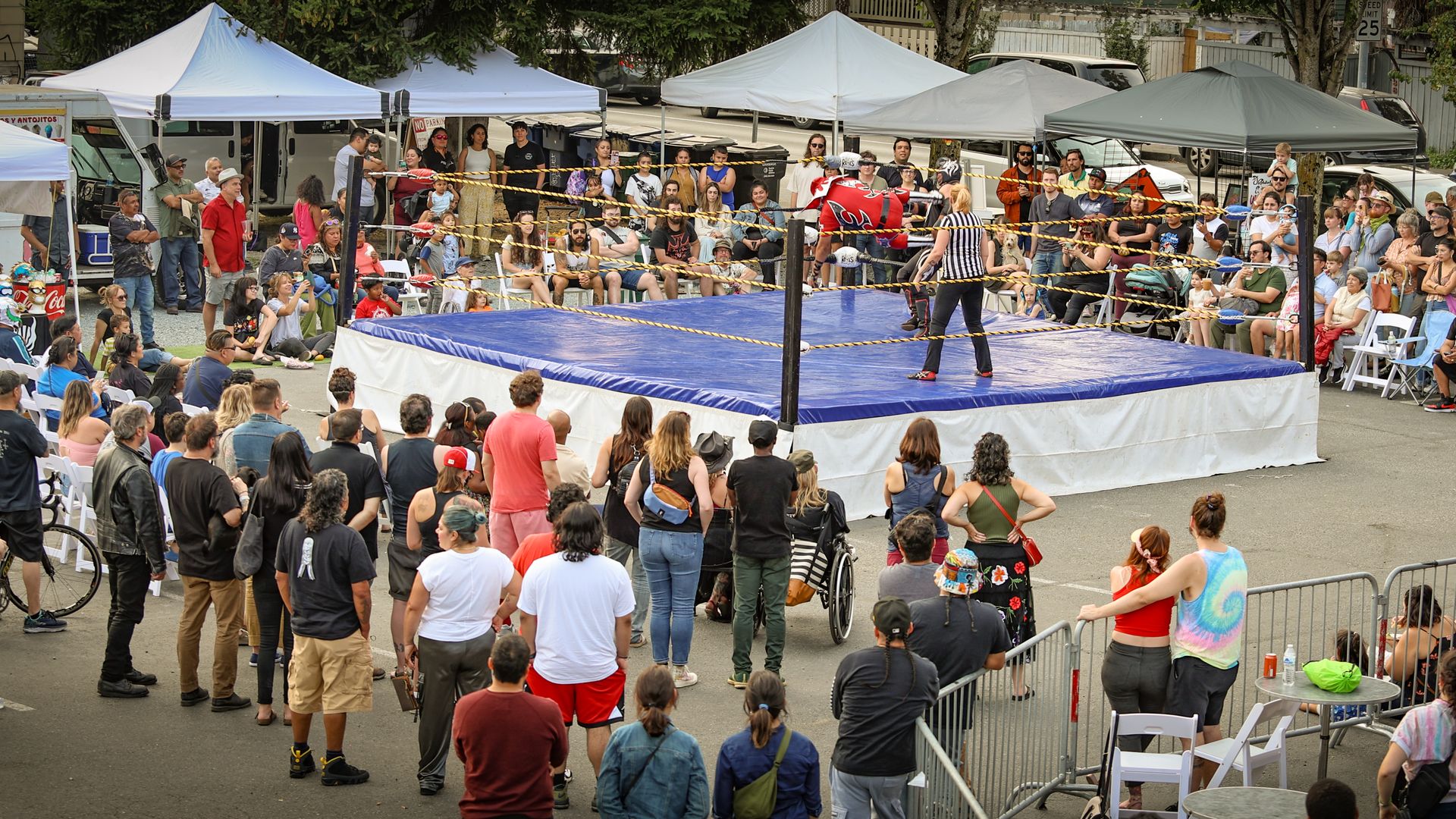 Spectators watch lucha libre wrestling on a blue mat stage.