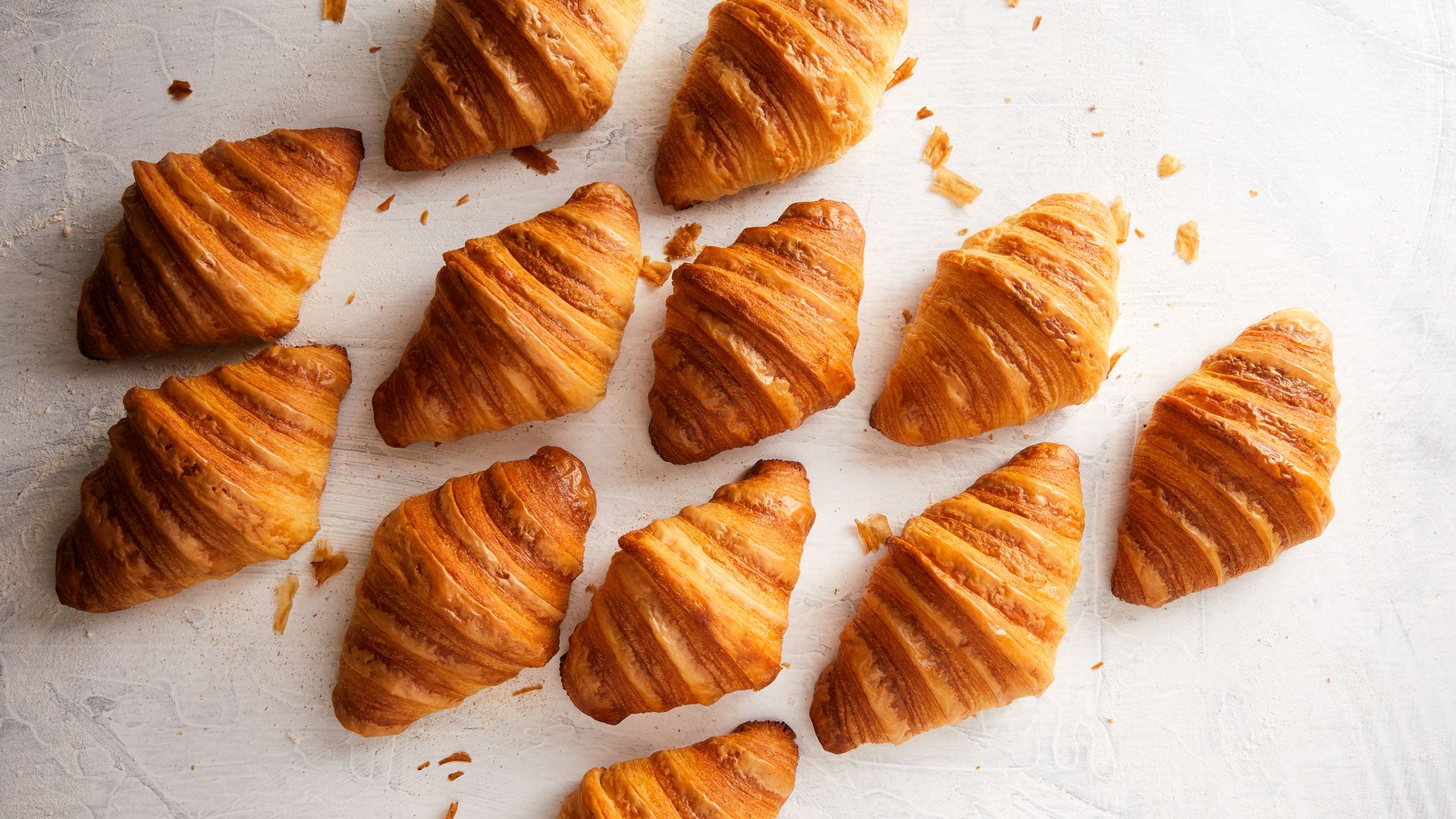 A marble countertop is filled with freshly baked croissants, viewed from above.