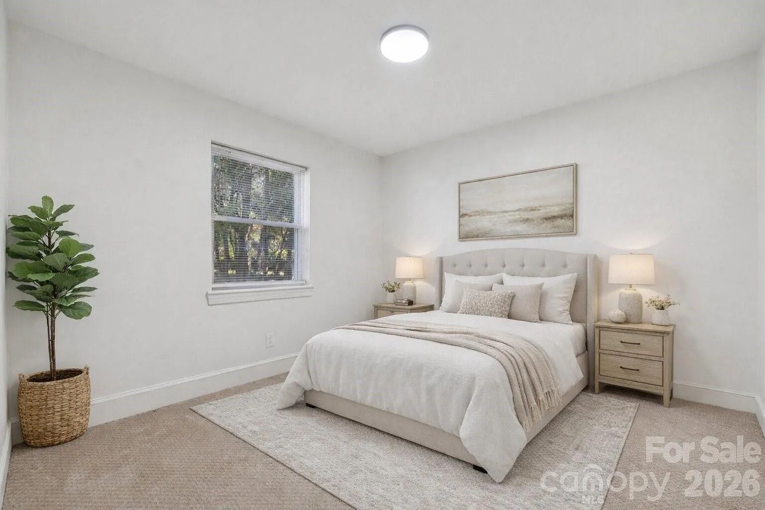 Minimalist bedroom with beige carpet, light gray bed with white and beige pillows, beige blanket, two wooden nightstands with lamps, large window, potted green plant, abstract landscape artwork.