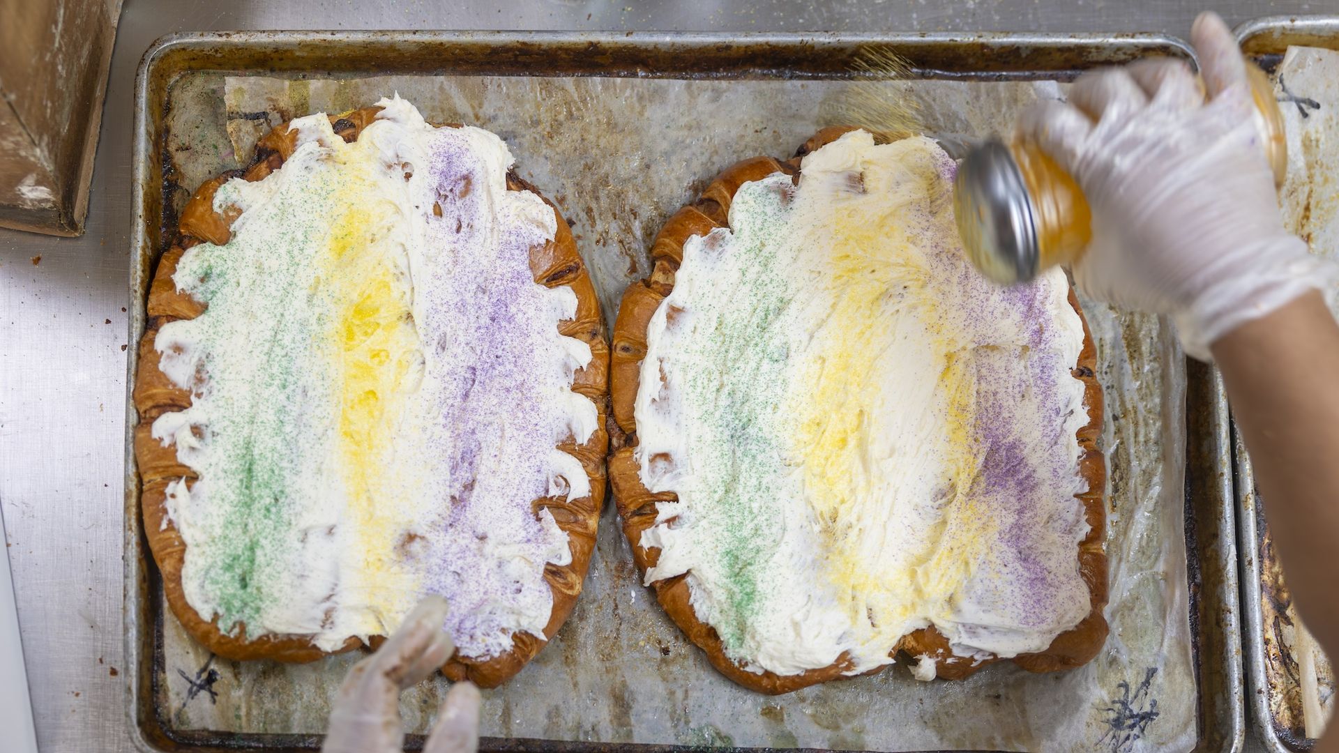 A baker shakes sprinkles on a king cake.