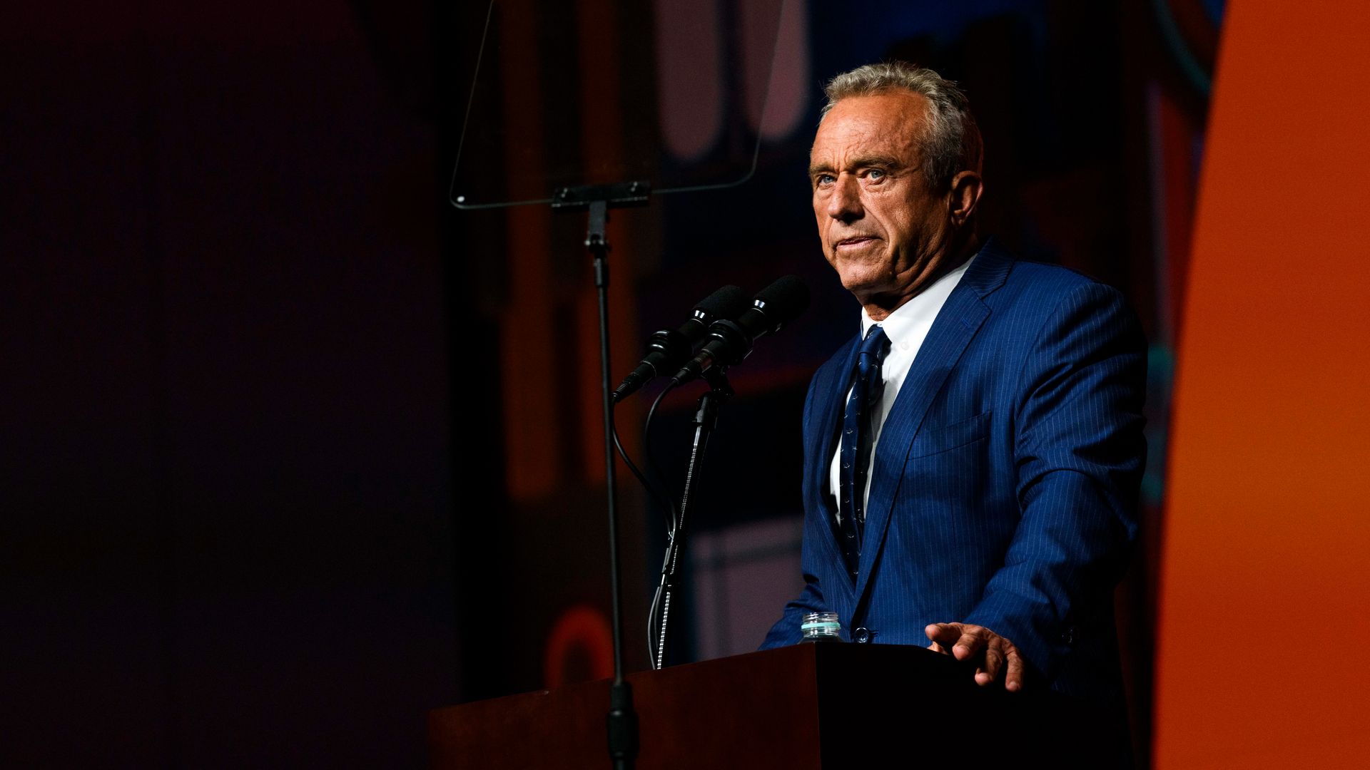 A man in a blue suit looks out at a crowd from behind a lecturn