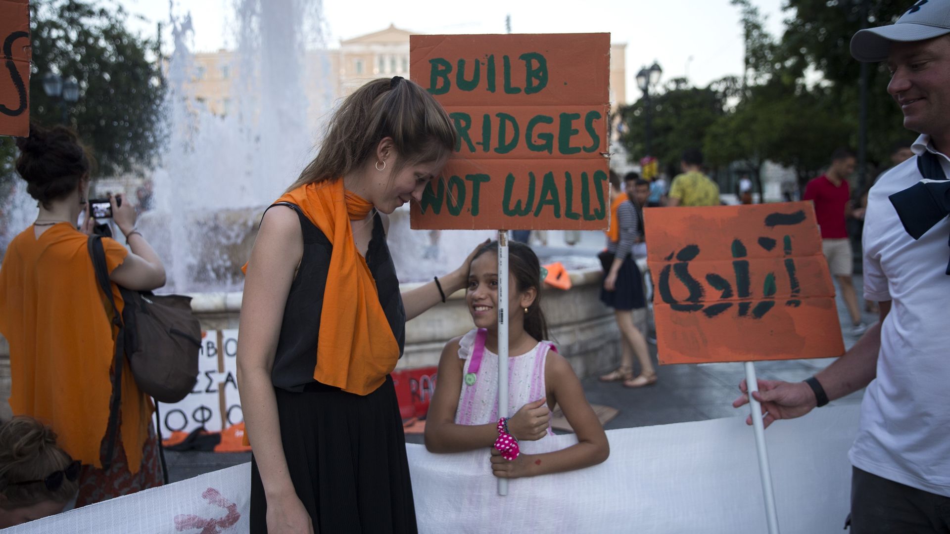 A little girl holds a sign that reads, "Build bridges not walls" 