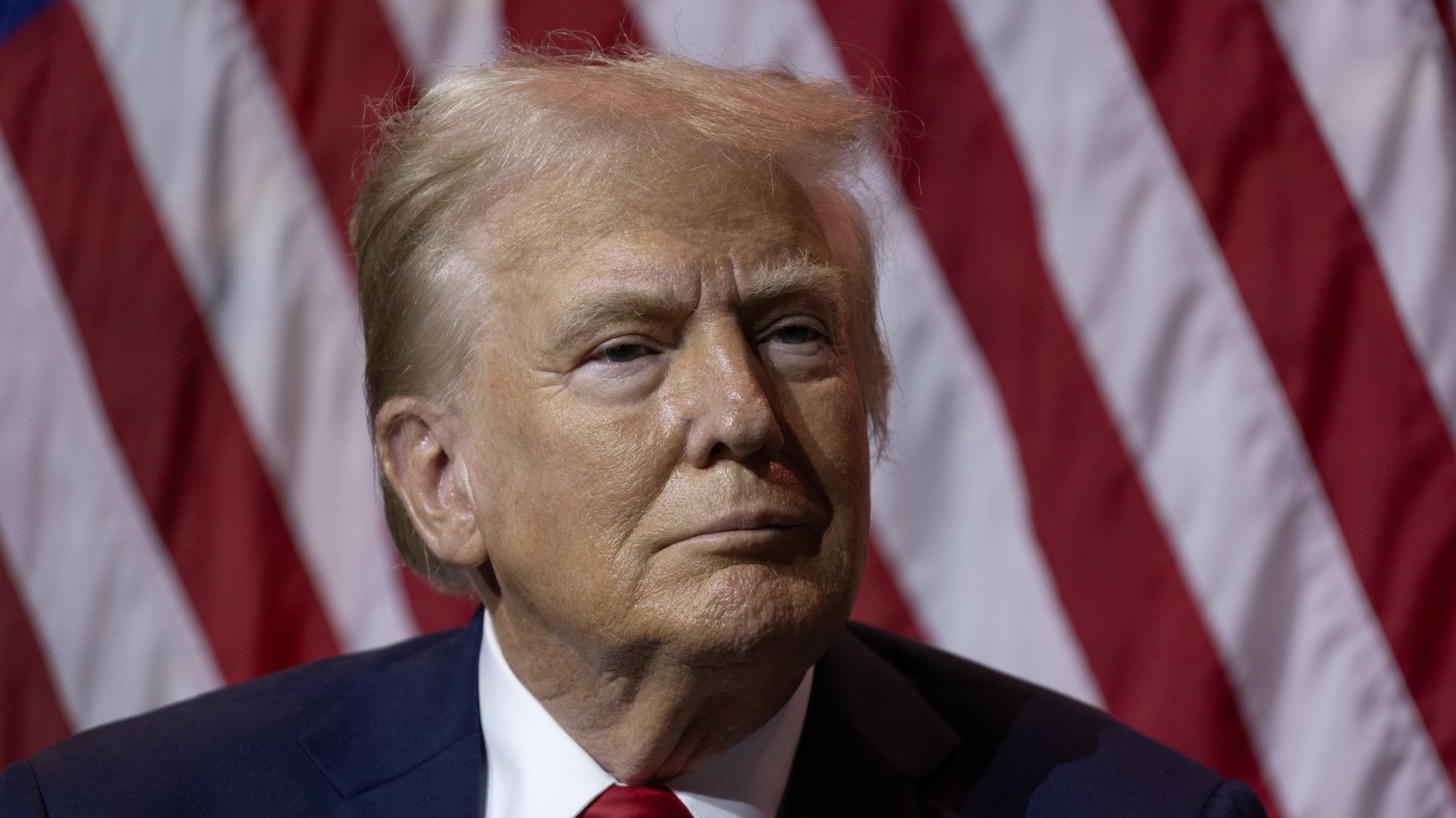 Trump looks on in front of an American flag.