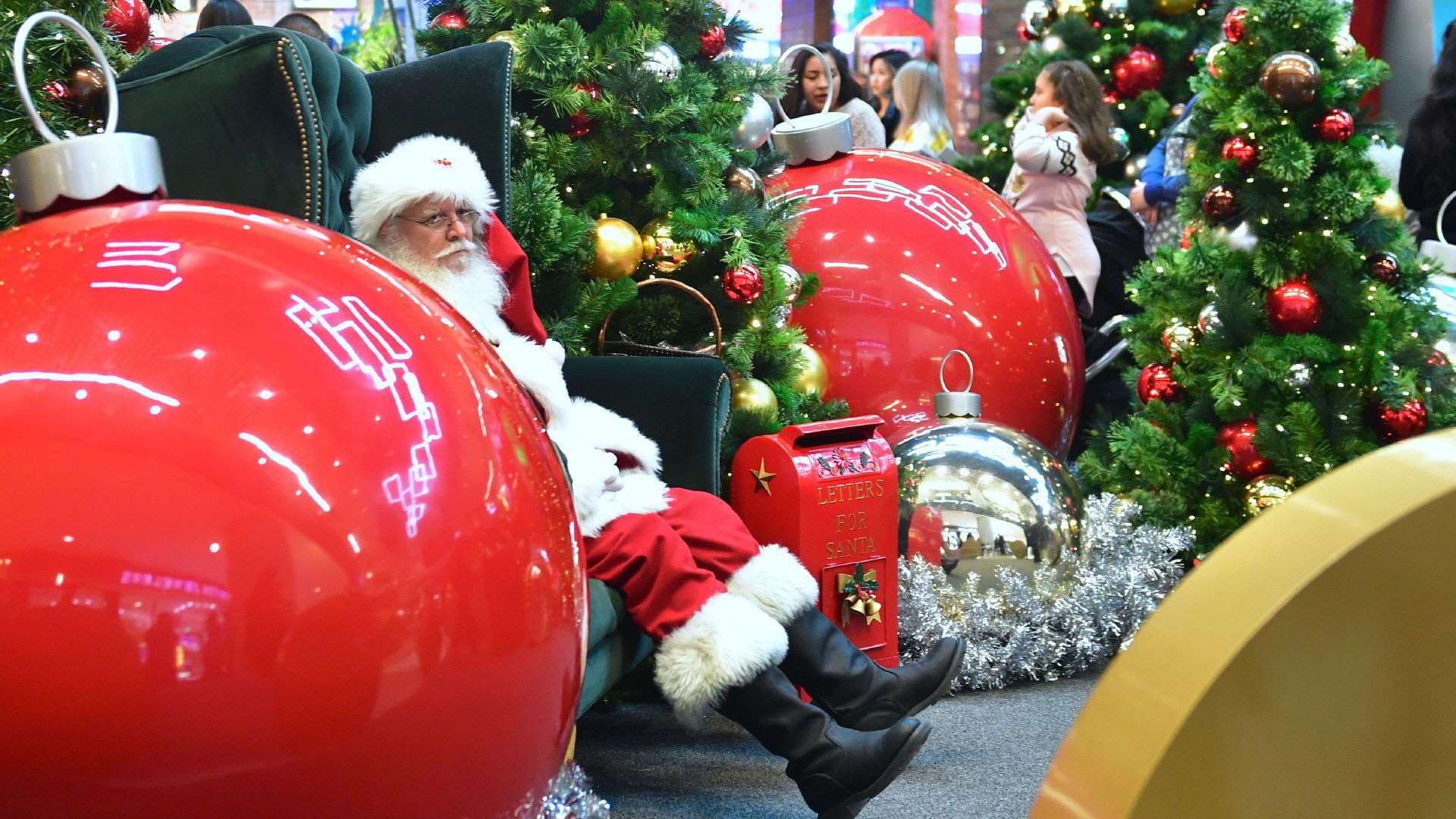 A sad looking Santa sits in a Christmas area of a shopping mall