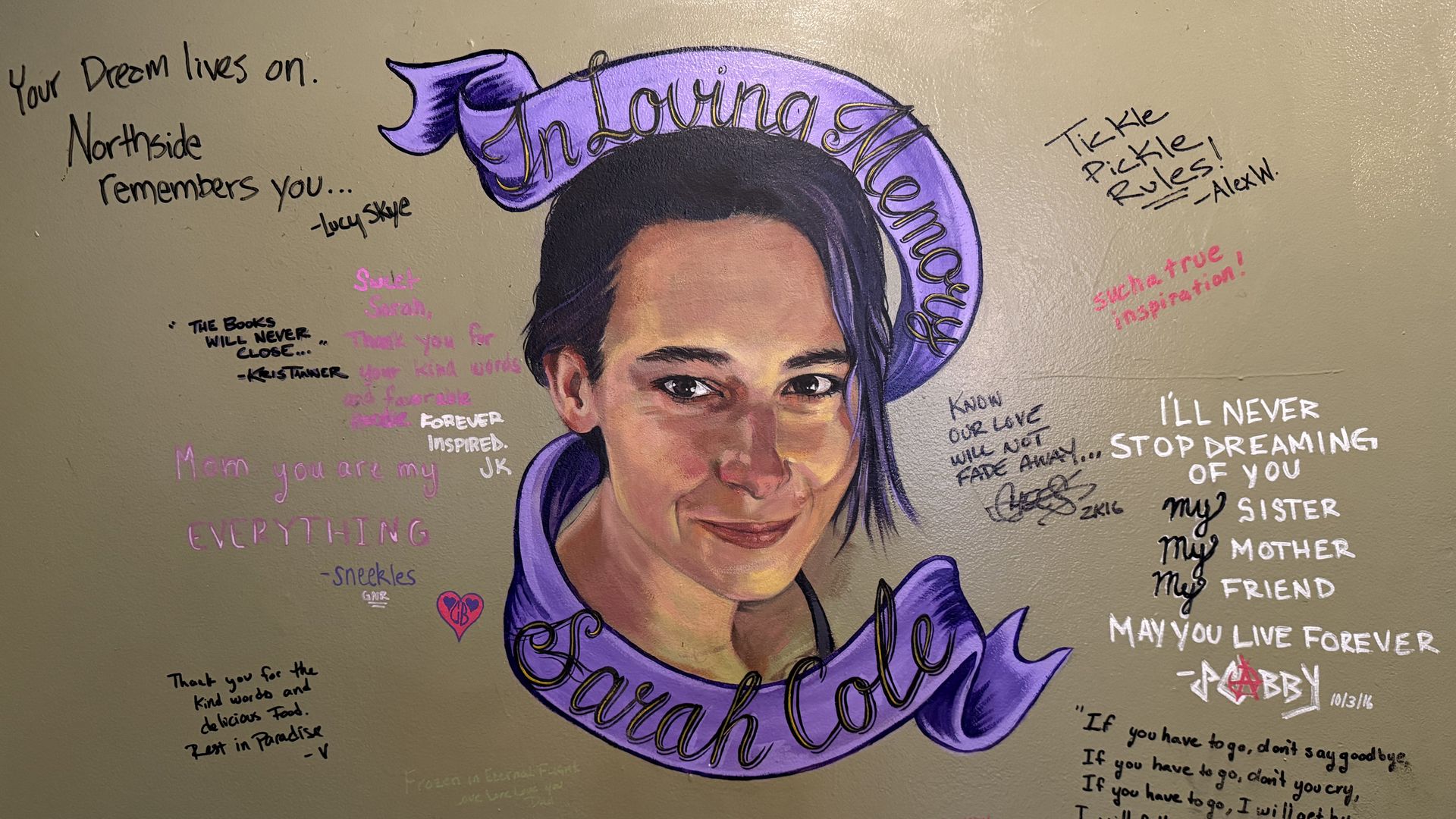 Graffiti mural of a woman's portrait with a purple headwrap on a beige wall, surrounded by handwritten quotes in black, pink, and white.
