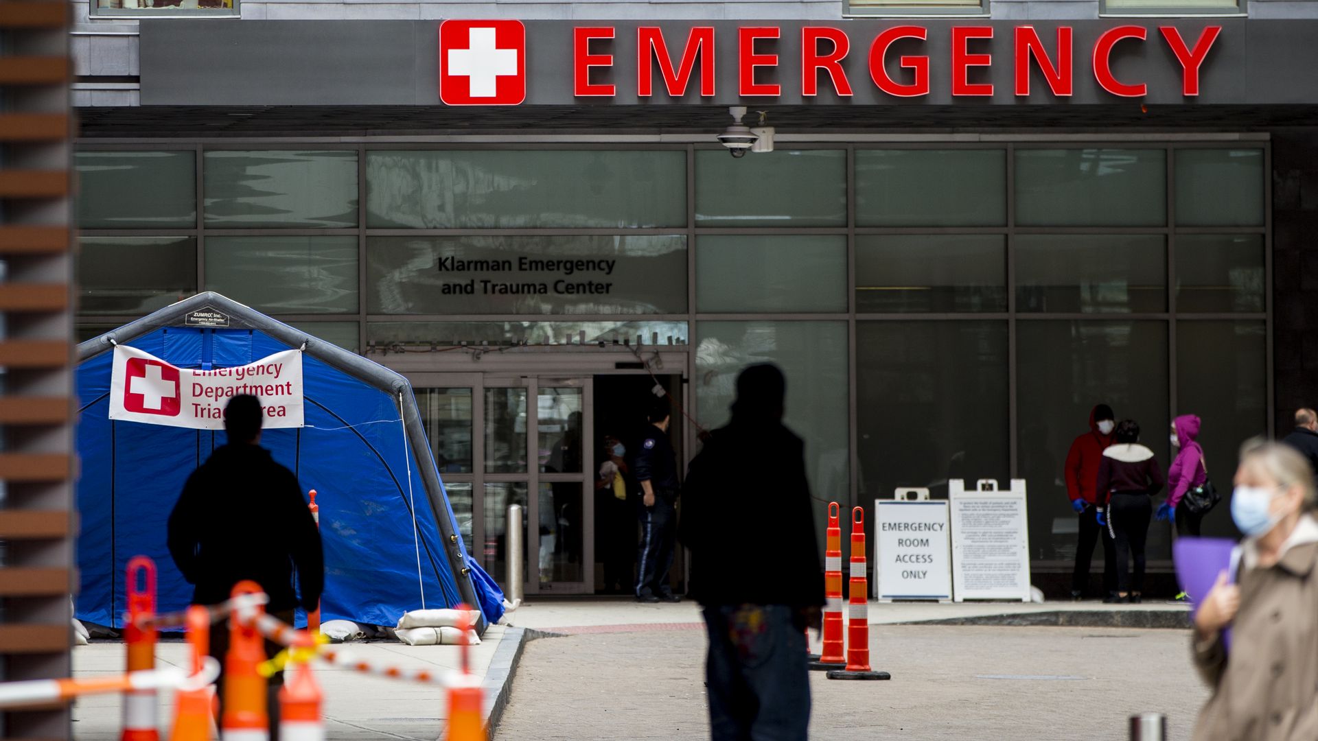 A hospital emergency building and white triage coronavirus testing tent, with workers standing nearby.