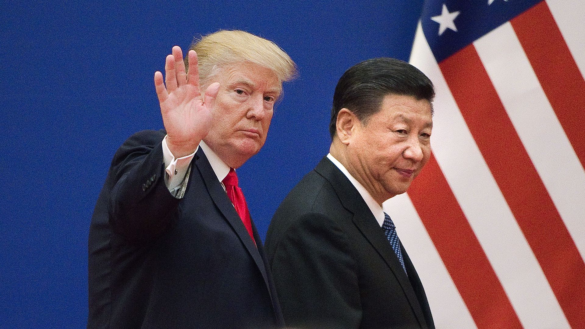 In this image, Trump and China's leader walk in the same direction towards an American flag while both wearing suits.