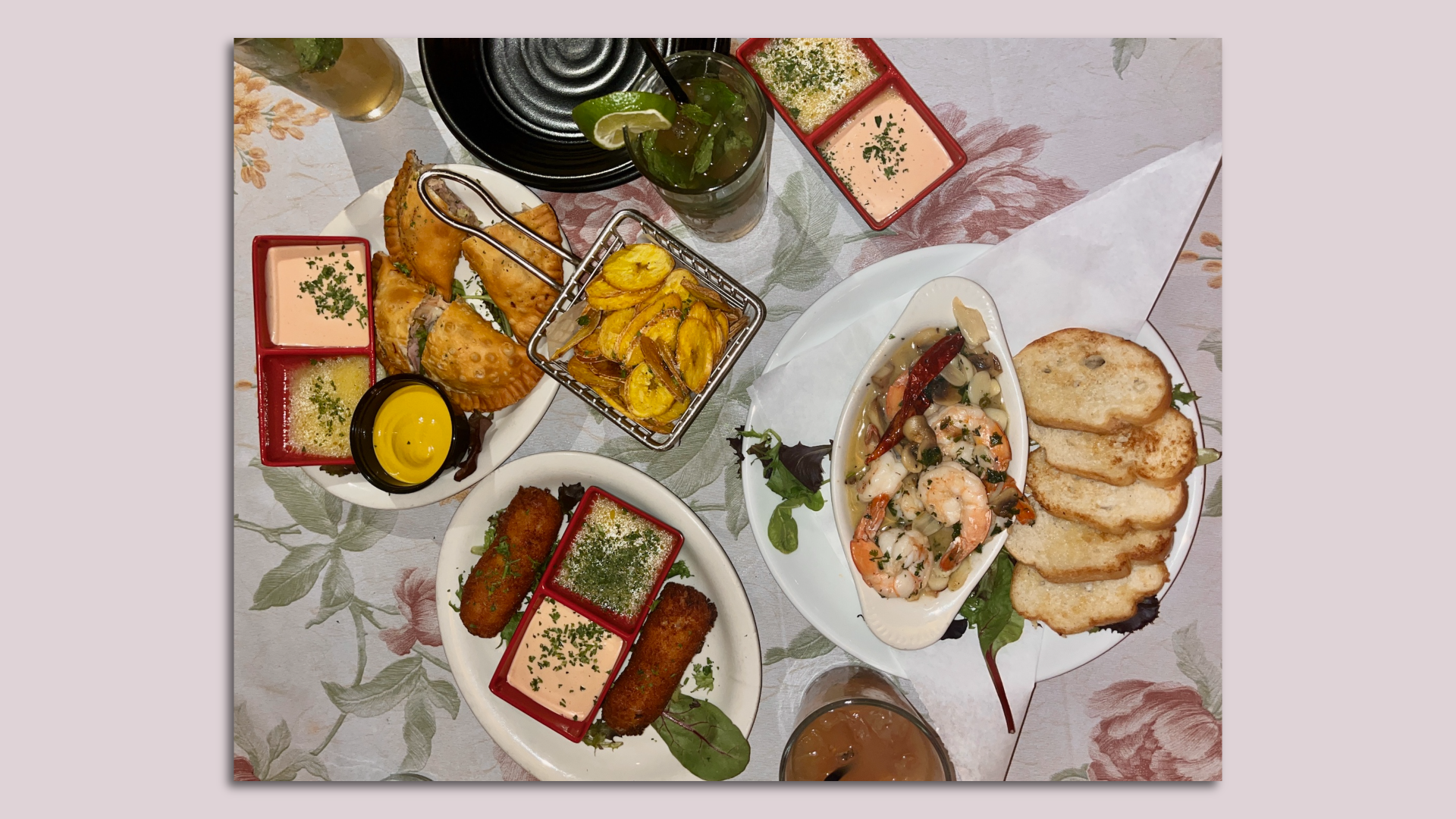 A table of Cuban dishes, including empanadas, croquettes, plantain chips, shrimp in garlic sauce and a mojito.