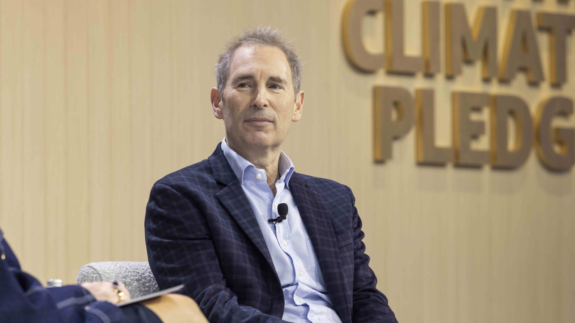 photo of Amazon CEO Andy Jassy sitting a suit on stage with 'climate pledge' in background