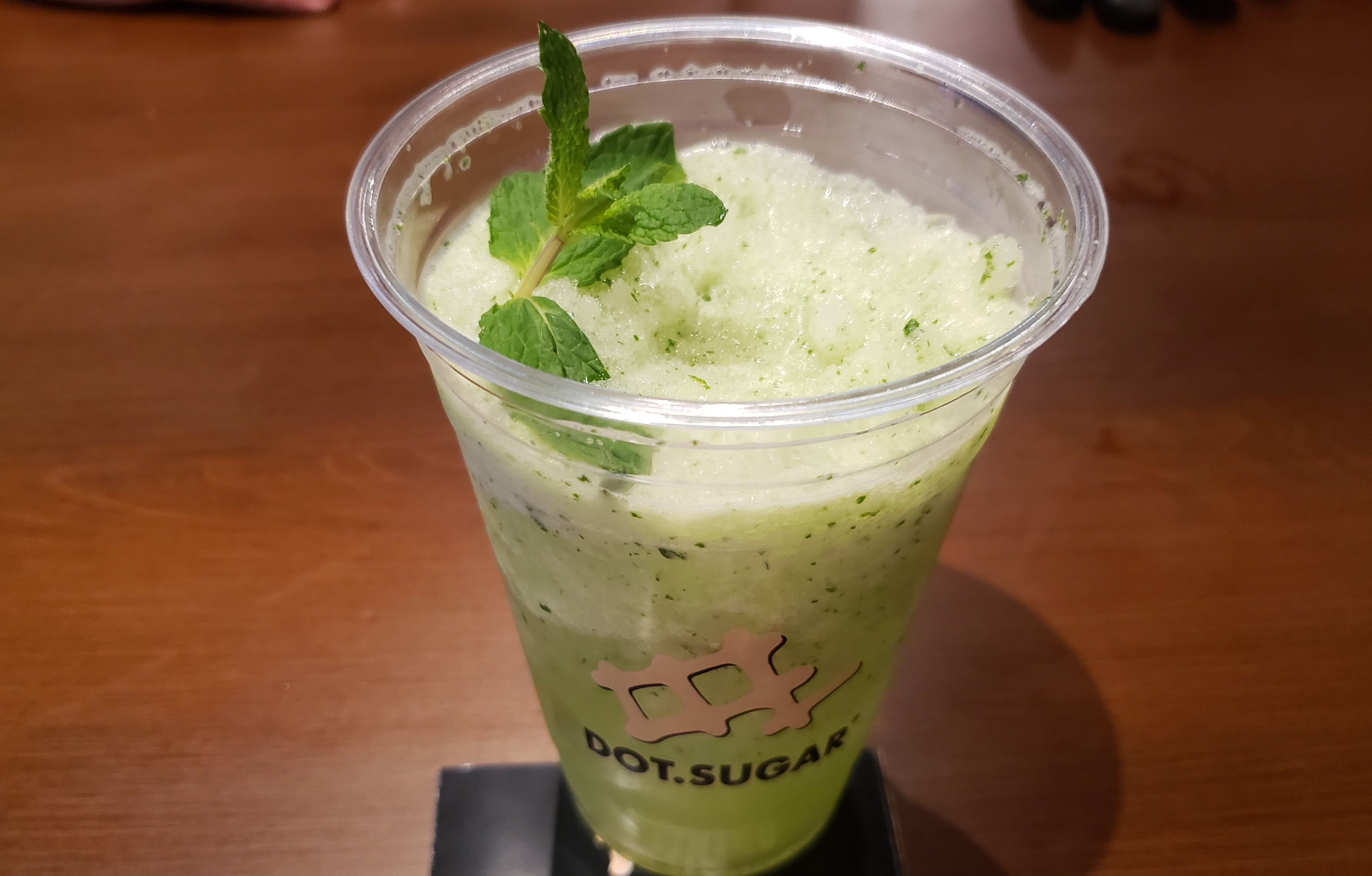 Green frozen drink with fresh mint in clear plastic cup.