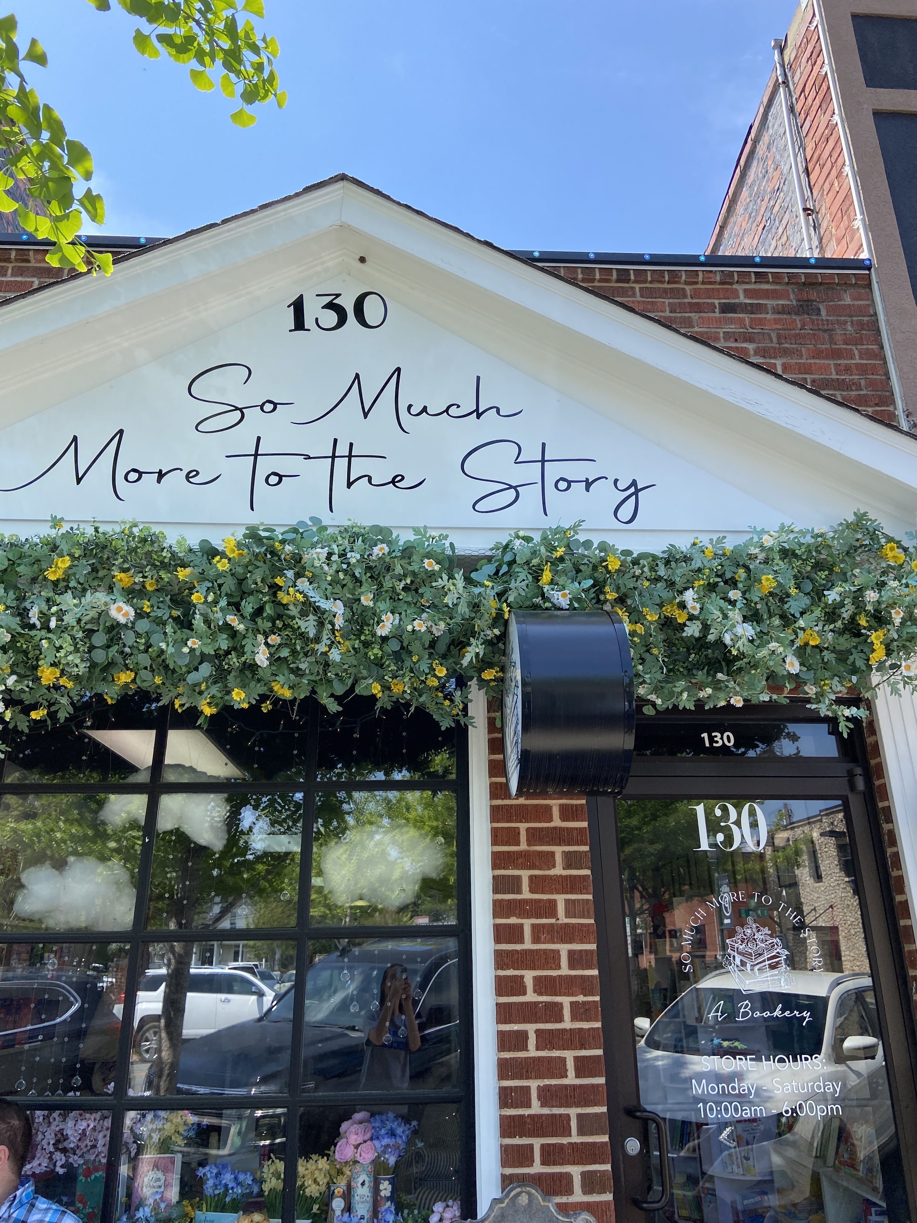 Entrance to So Much More to the Story bookshop in Monroe. The brick building has yellow and white flowers beneath the sign bearing its name. 