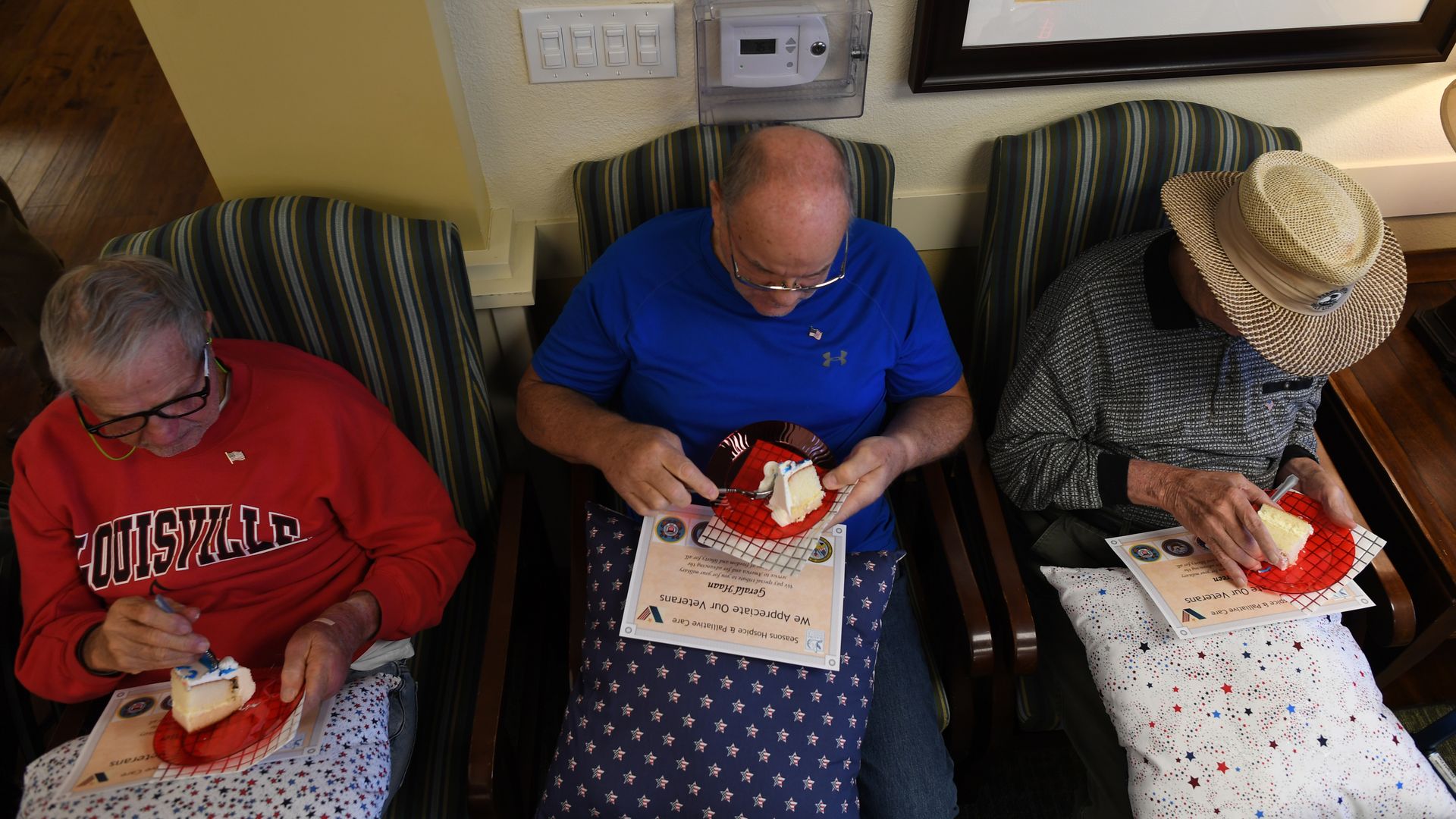 In this image, three seniors sit and eat cake. A few have blankets over their laps.
