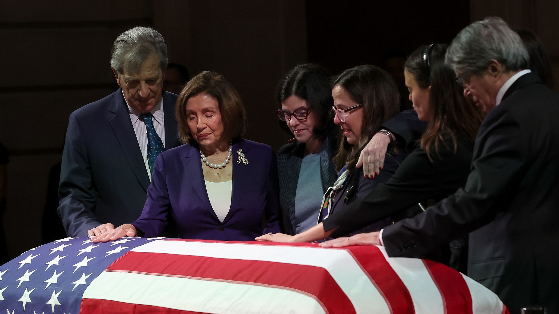 Paul Pelosi, Nancy Pelosi and others stand with a hand on Feinstein's casket, which is wrapped in an American flag.