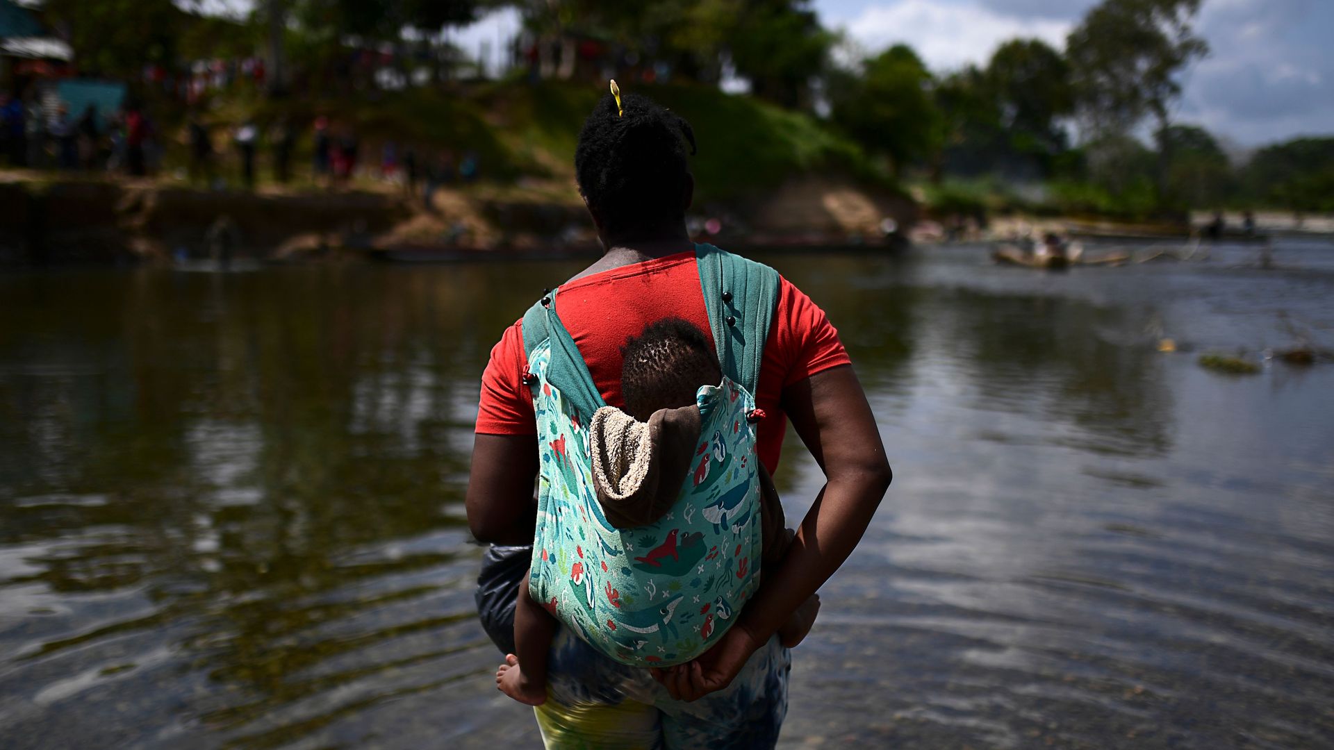 A migrant carrying a baby crosses the Chucunaque river after walking for five days in the Darien Gap, in Bajo Chiquito village, Darien province, Panama on February 10, 2021, on their way to the US.
