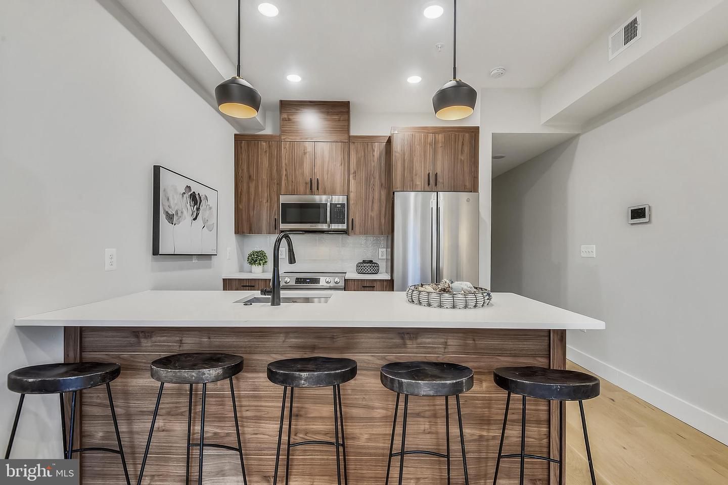 A kitchen with bar stools, white countertops, and dark wood cabinets.
