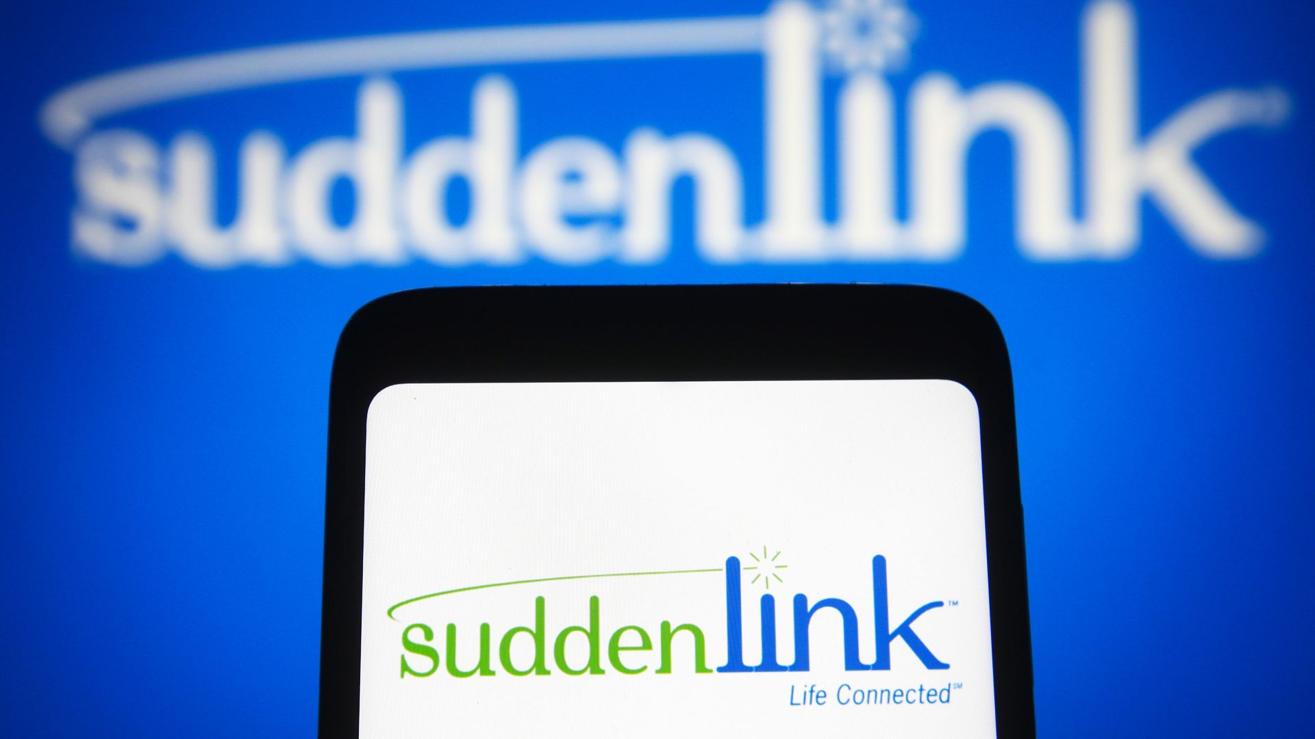 In this photo illustration, the Suddenlink Communications logo is seen displayed on a smartphone screen and in the background.