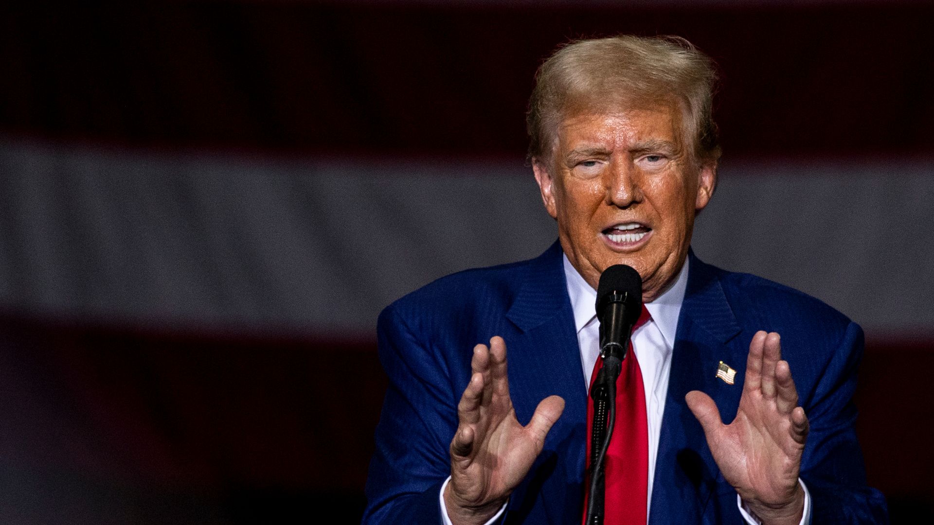 Trump speaks into a microphone with both hands in front of him. 