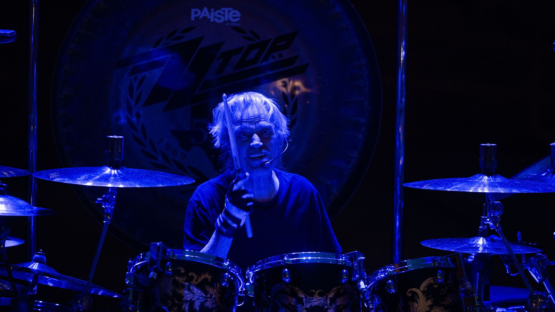 Frank Beard plays a drum set under blue stage lighting