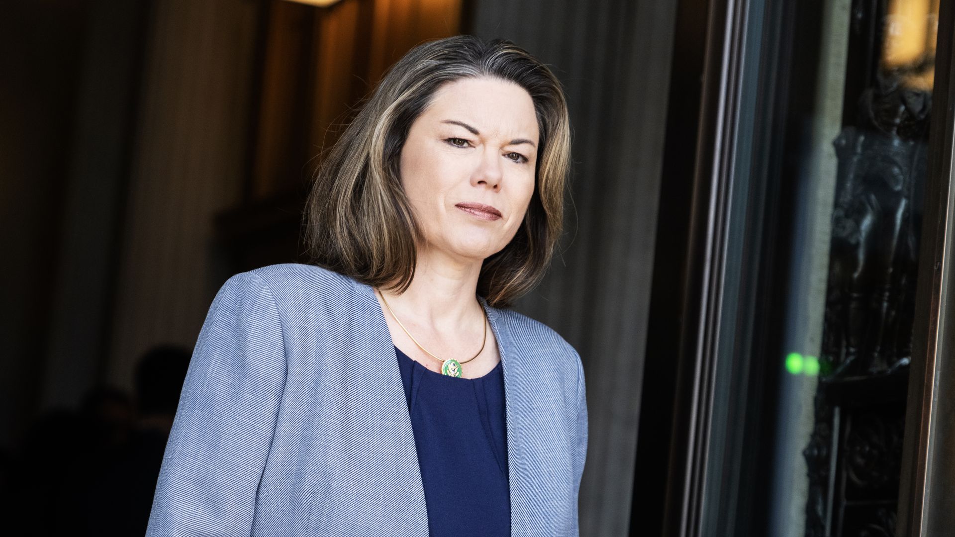 Rep. Angie Craig, wearing a baby blue blazer and standing in front of a black iron door.