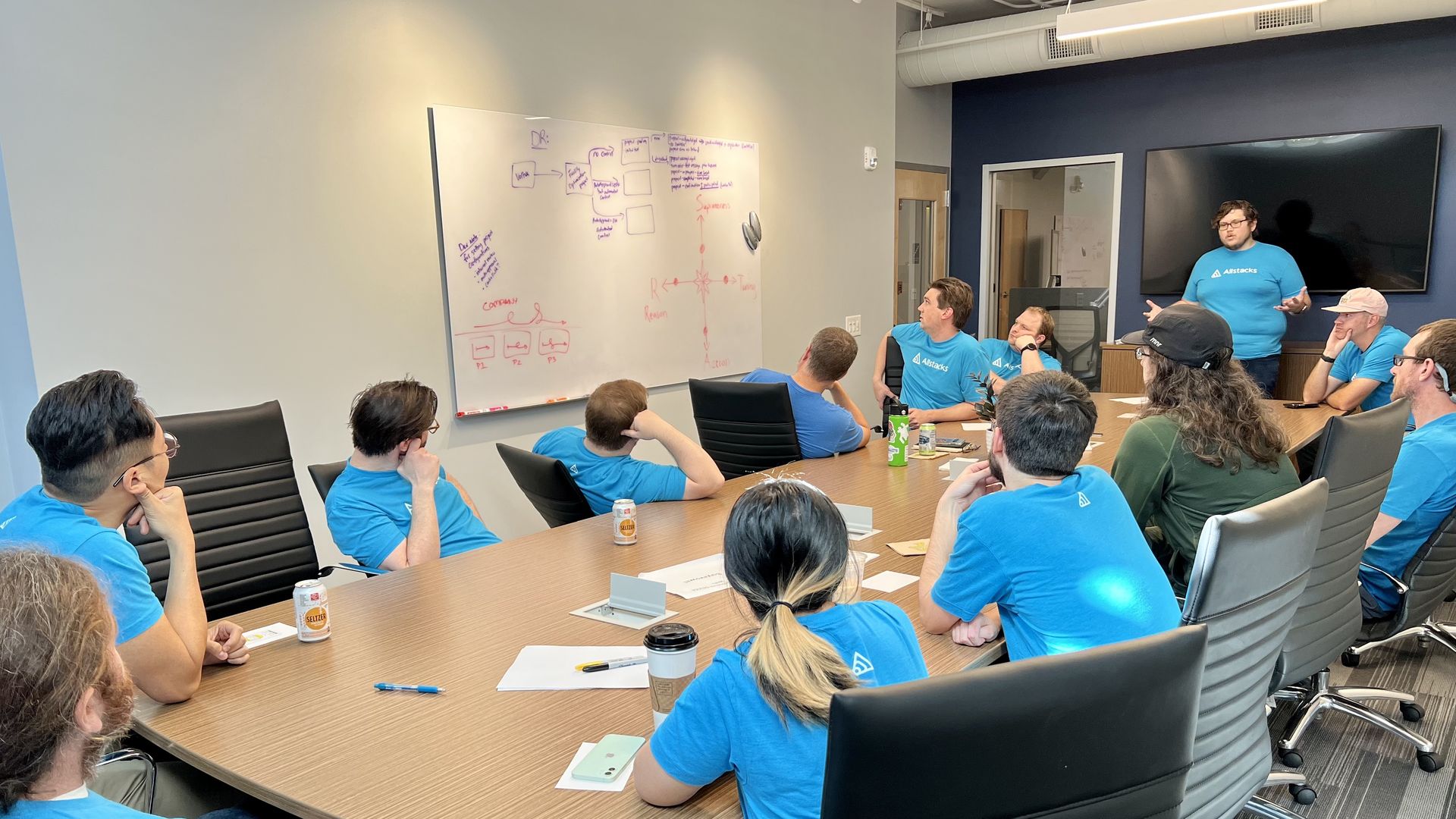 A group of software workers in matching blue shirts stare at a whiteboard. 